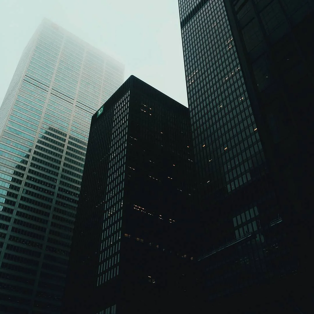 Low angle view of tall skyscrapers in a city, with a foggy sky overhead.