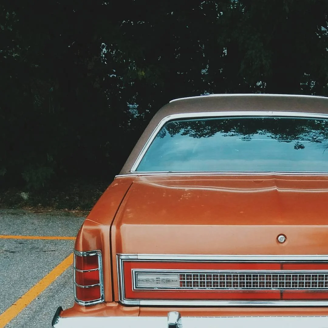 Rear view of vintage orange and brown station wagon parked on a parking lot with trees in the background.