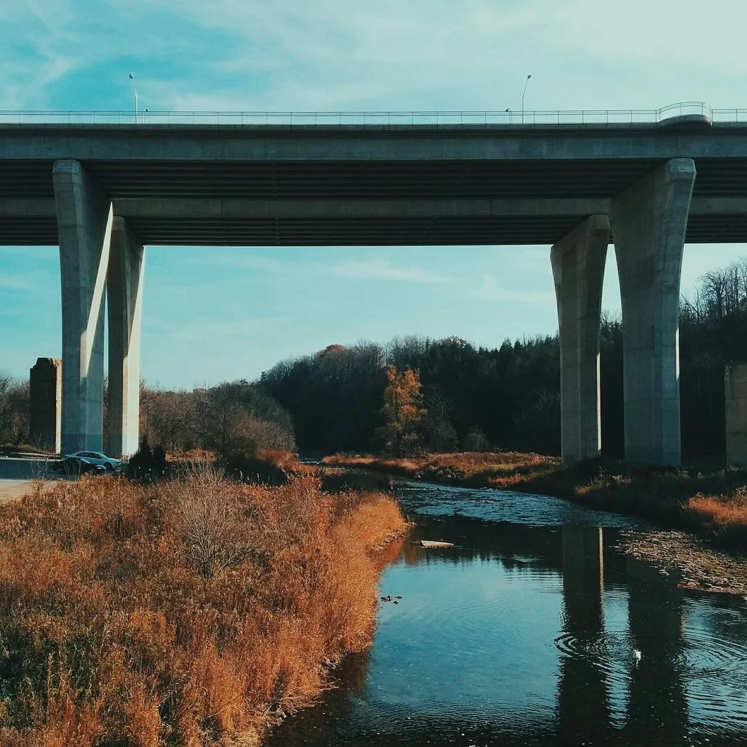 A concrete bridge spanning over a calm river with autumn foliage in the background.