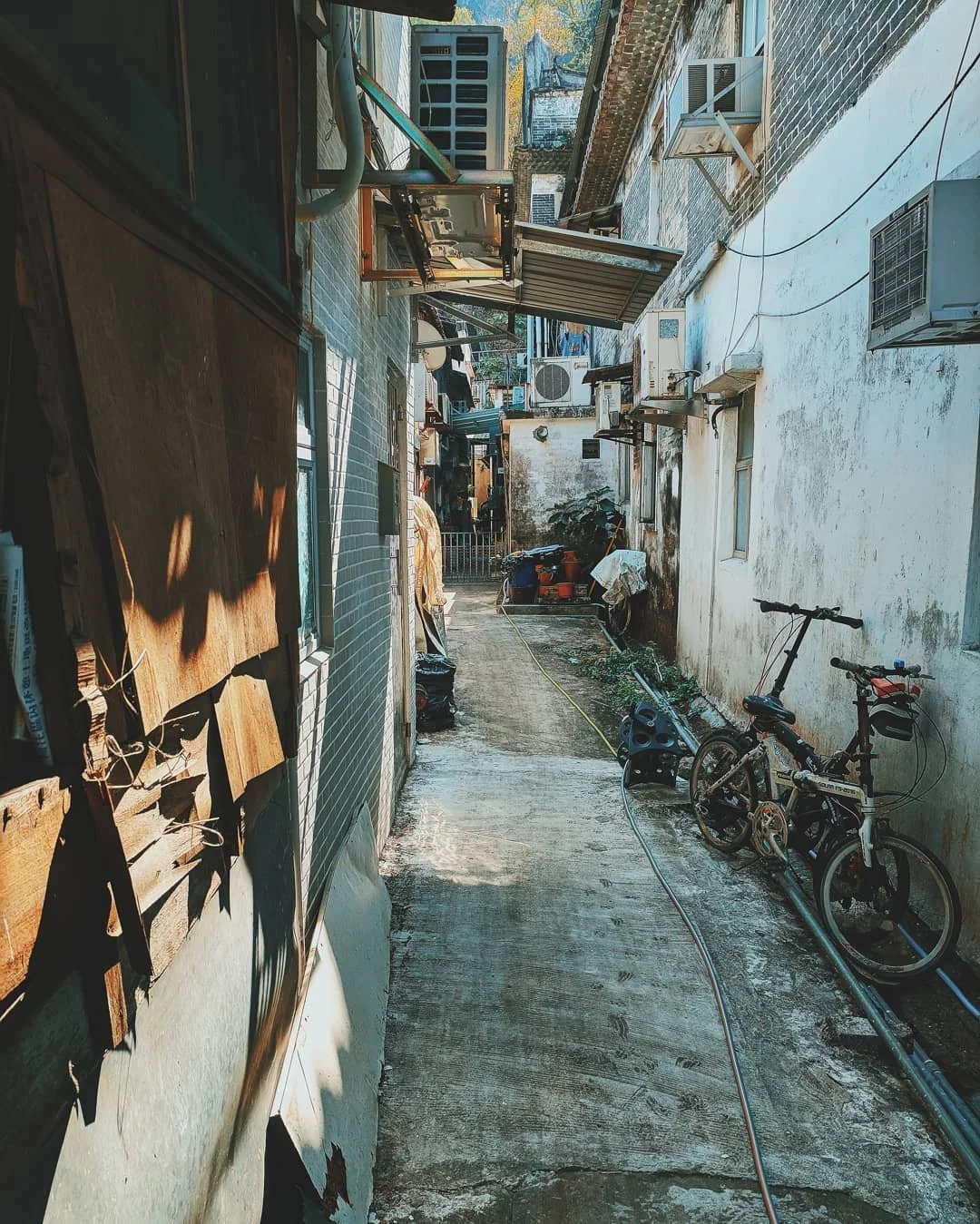 A narrow alleyway between buildings with various outdoor items, a bicycle, and an air conditioning unit on the wall.