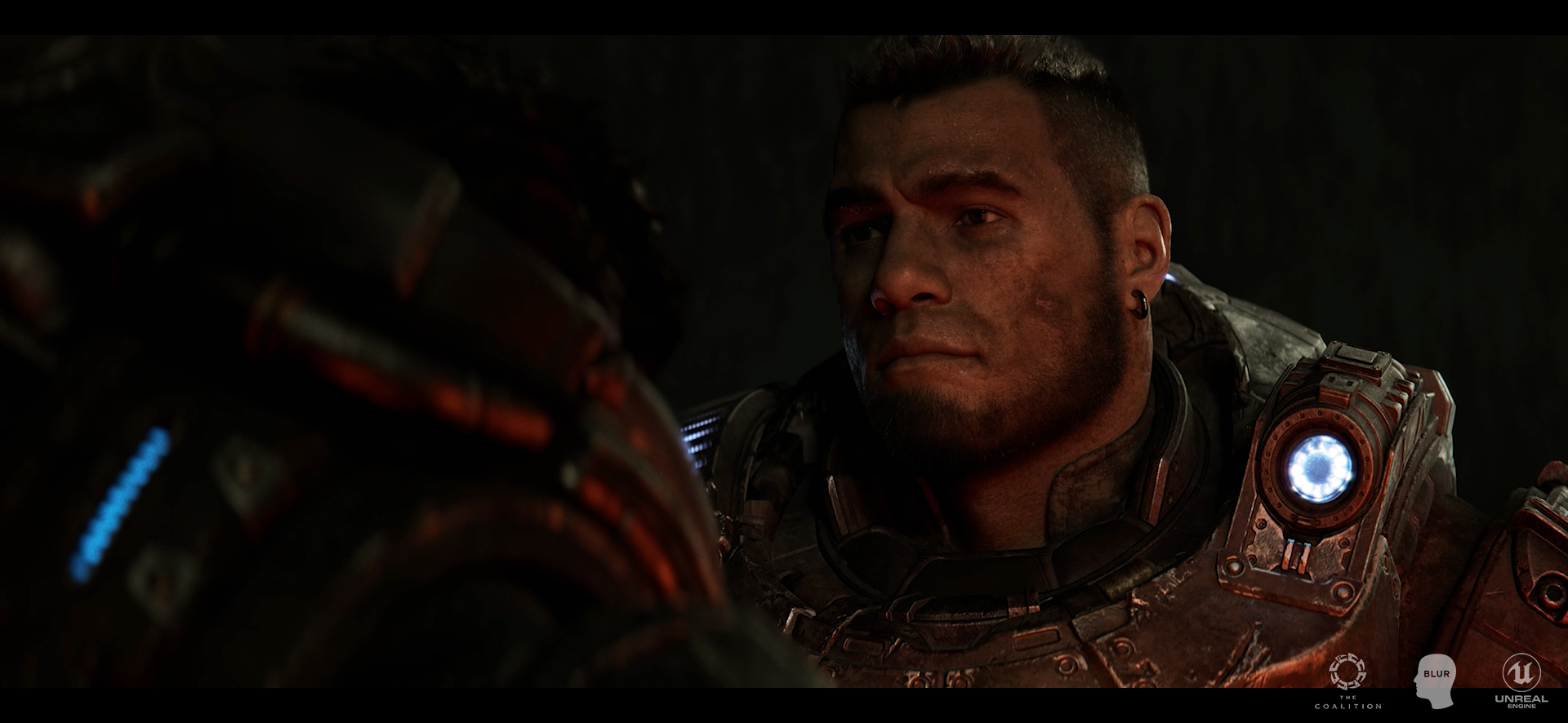 Close-up of a man in a futuristic space suit with a glowing circular element on the shoulder, looking intently at something in a dark environment.