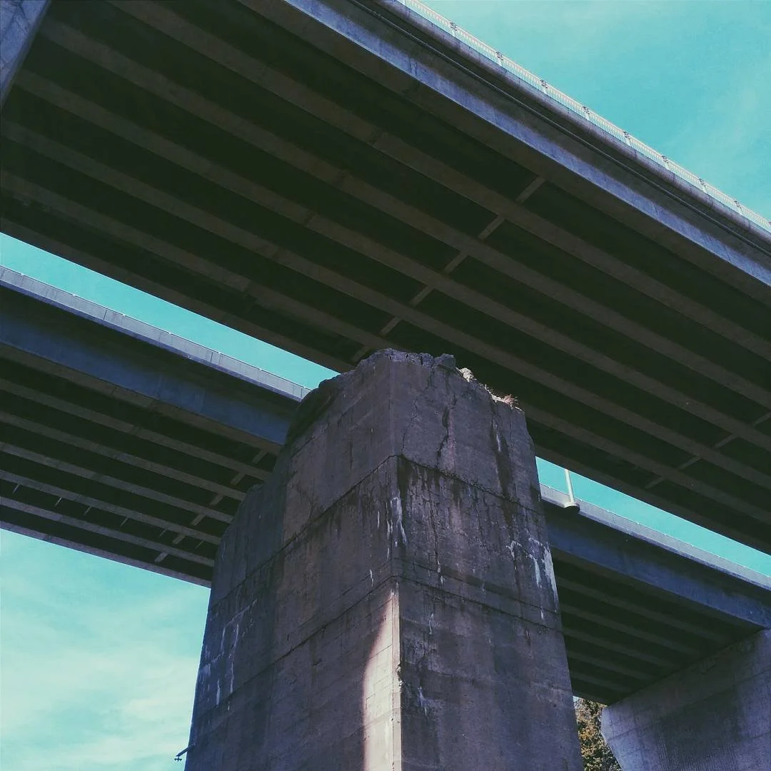 View of a concrete bridge pier supporting two levels of a highway or overpass, with the underside of the bridges visible against a blue sky.