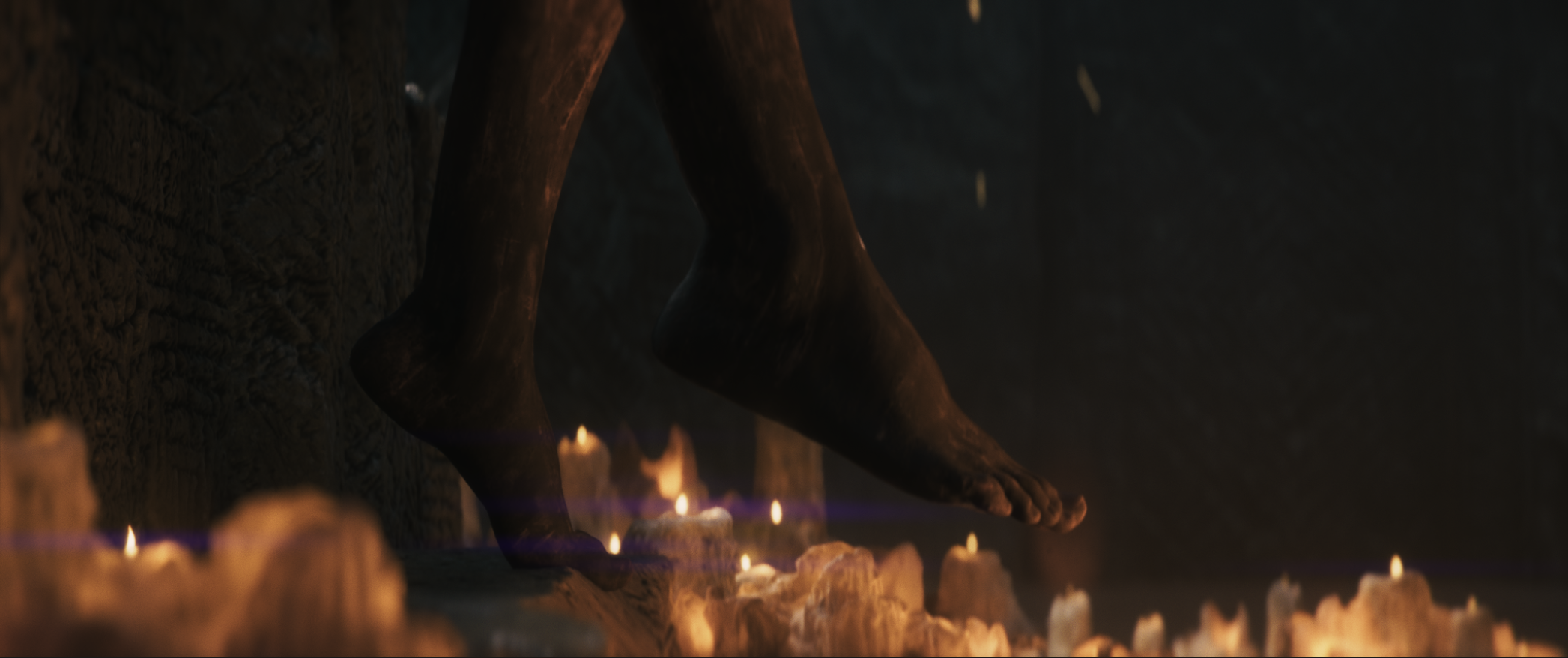 Close-up of a carved wooden foot statue surrounded by lit candles in a dark, atmospheric setting.