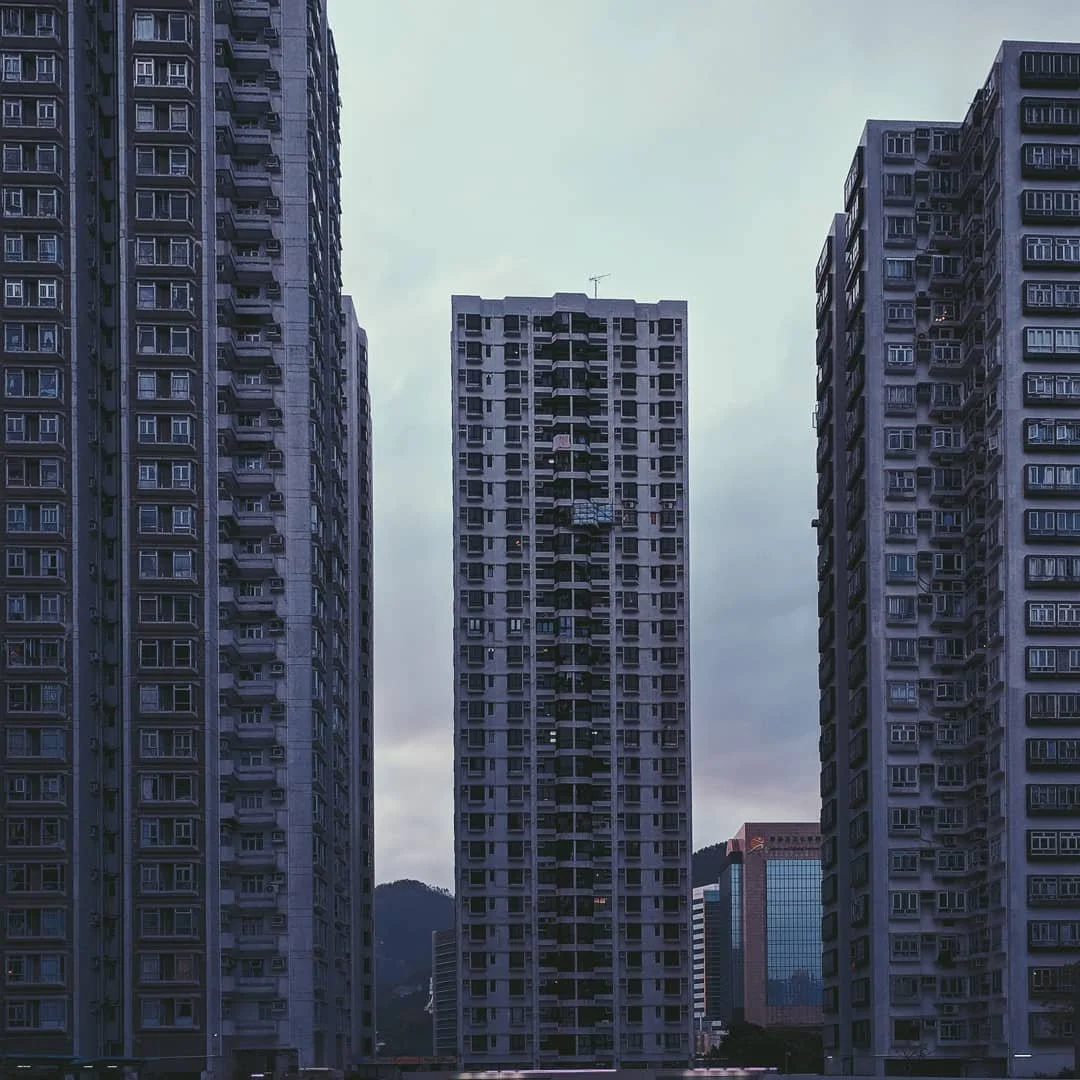 Three tall apartment buildings against a cloudy sky with a mountain in the background.