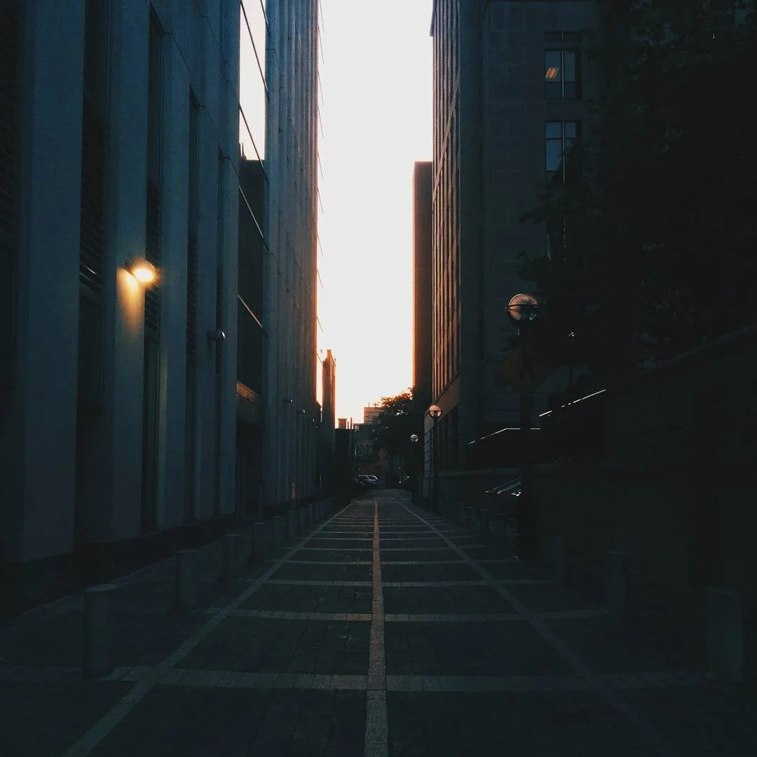 Empty city street at sunset with tall buildings on both sides and a narrow walkway