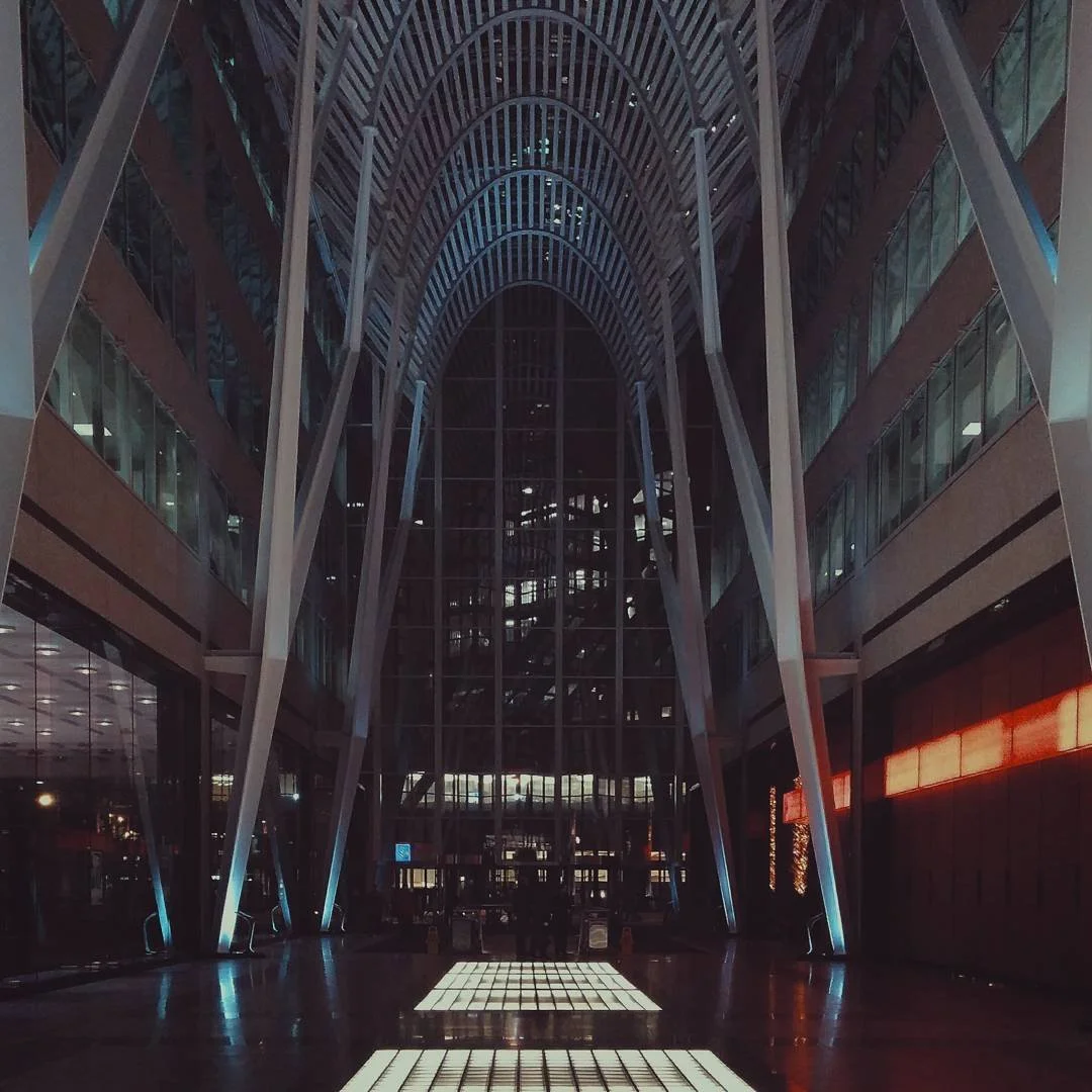 Interior view of a modern building with tall glass windows and architectural steel beams forming an arched ceiling.