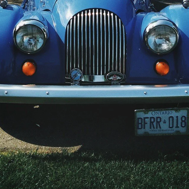 Close-up of front of a blue vintage car with a chrome grille, round headlights, orange turn signals, and an Ontario license plate reading 'BFR 018'.