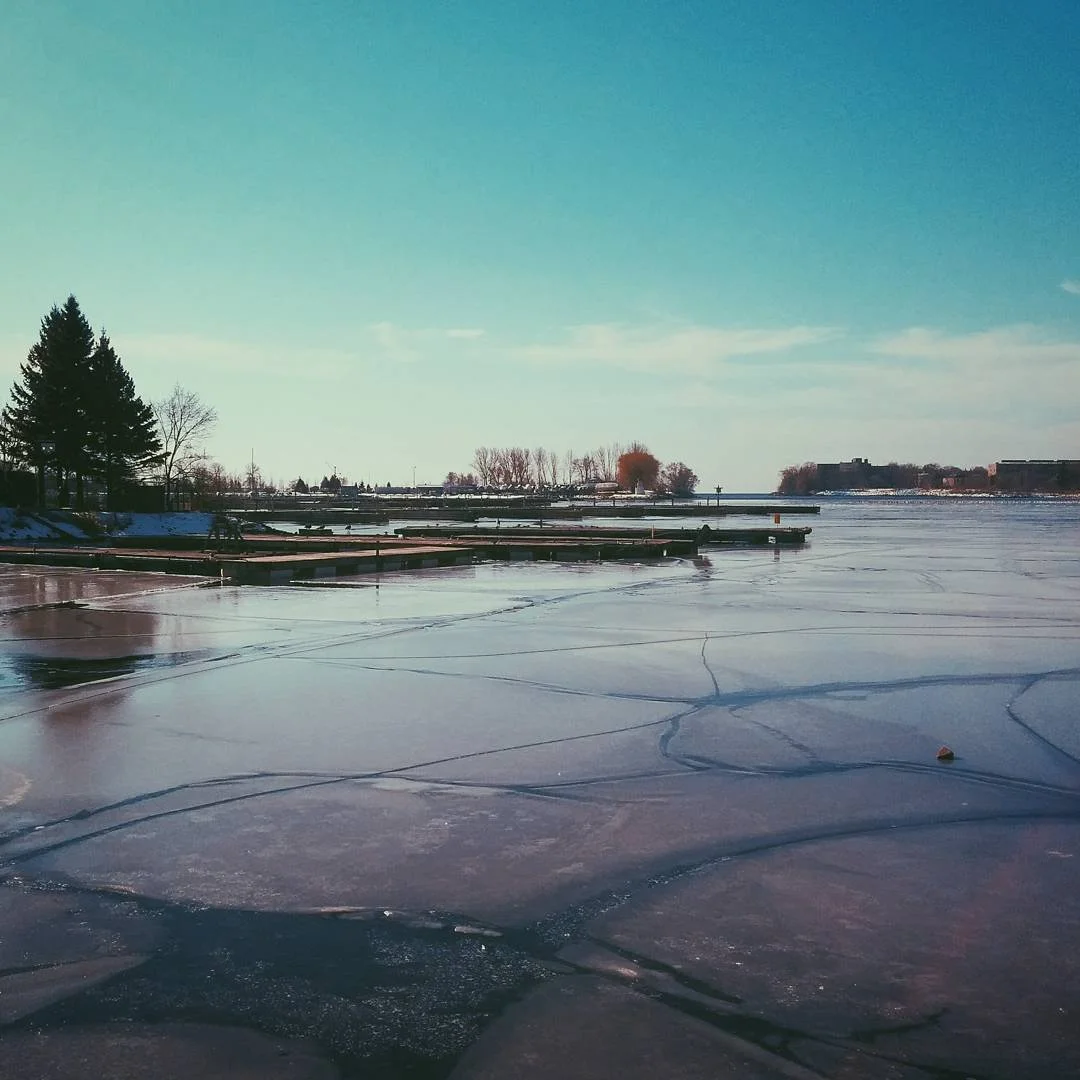 Frozen lake with docks and trees in the background, partly cloudy sky.