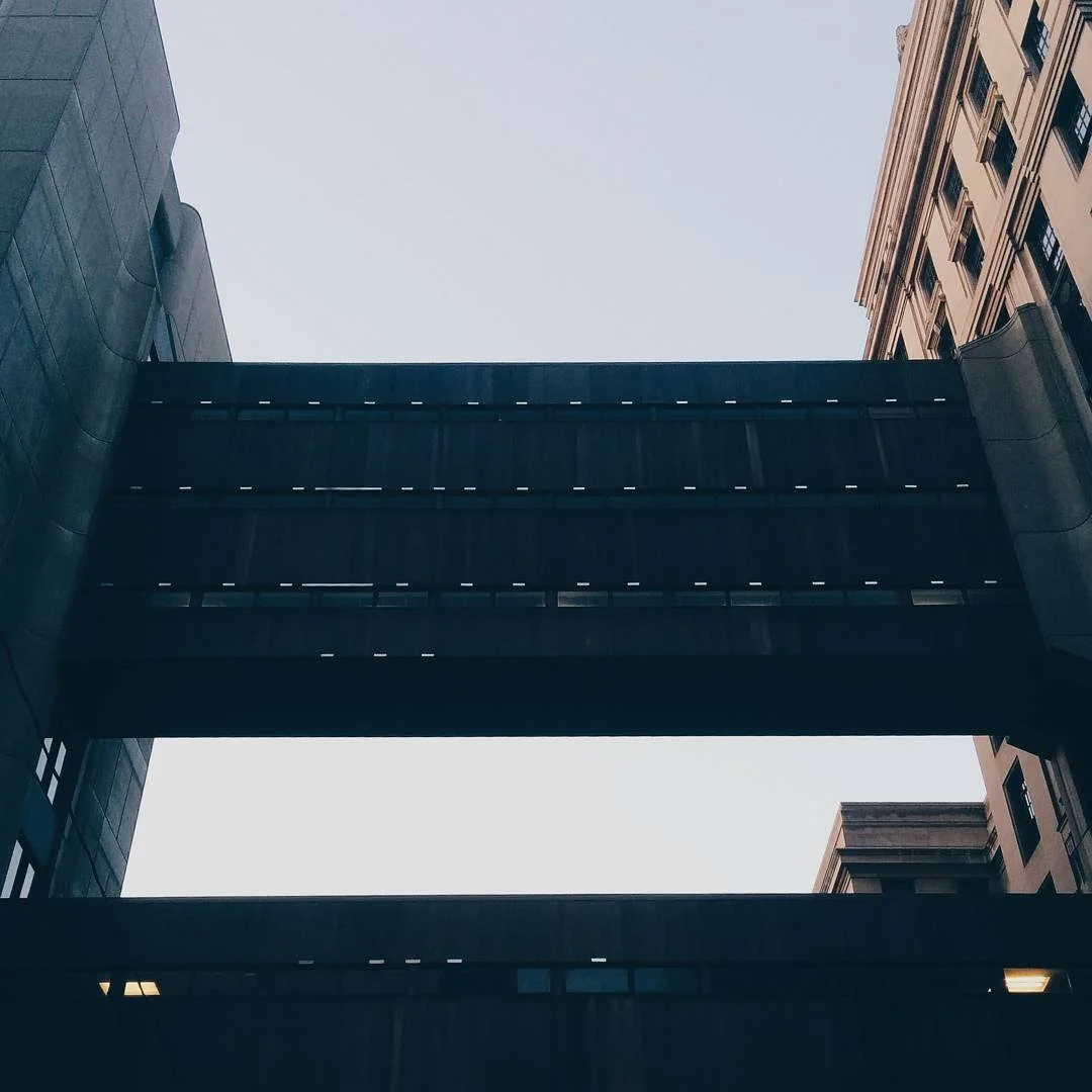 View of a modern building with a skywalk bridge connecting two buildings, captured from below against a clear sky.