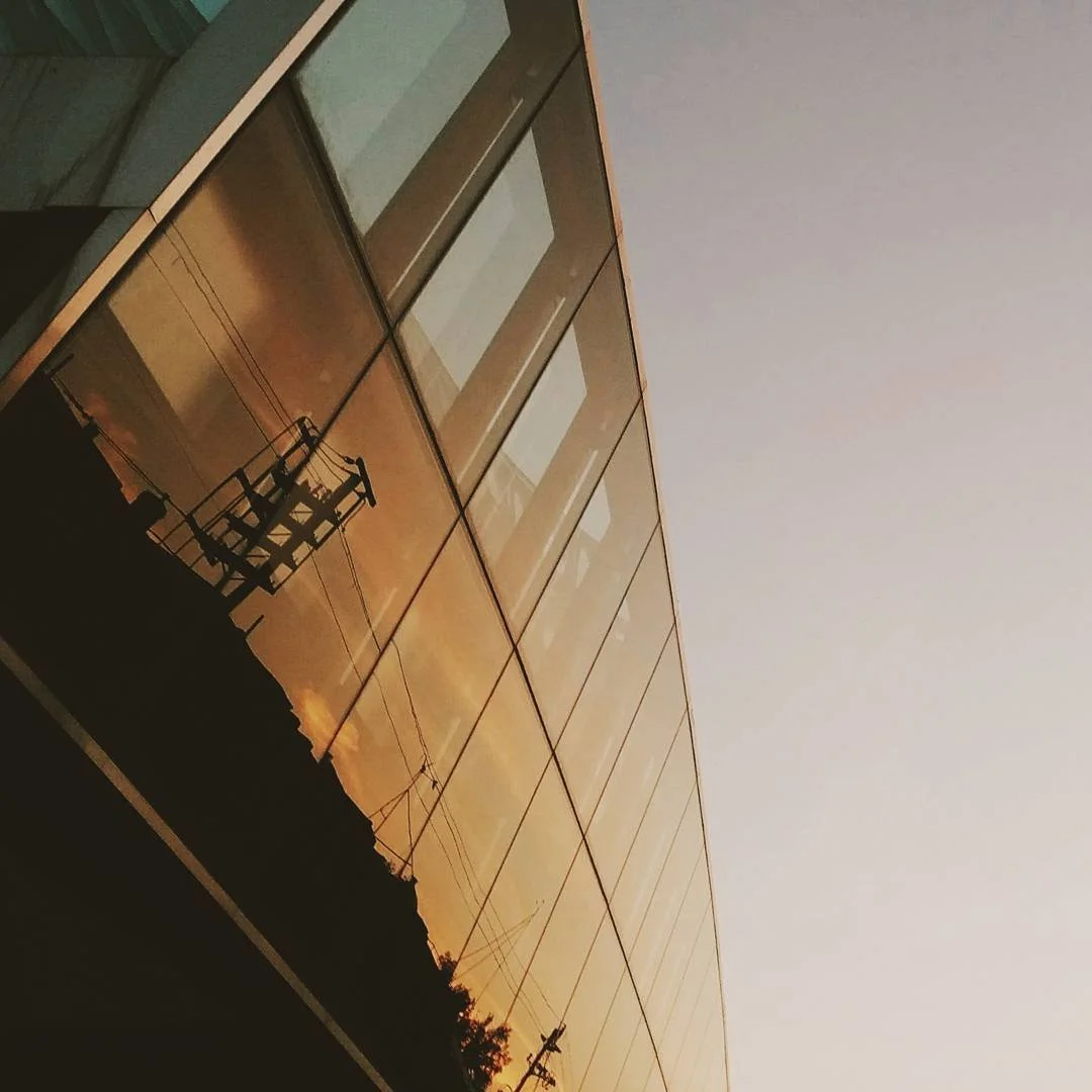Sunset reflecting off the window of a modern building, with a power line and silhouette of trees in the foreground.
