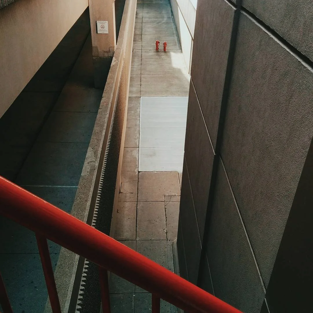 View of an outdoor building corridor with concrete and tile flooring, red fire hydrants, and a red railing in the foreground.