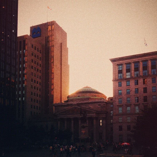 Sunset over a city skyline with tall buildings and a historic courthouse in the foreground.