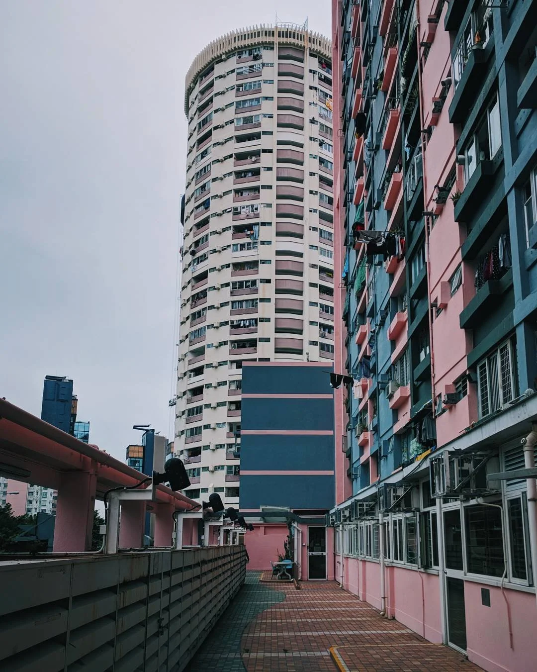 View of tall residential buildings with balconies, laundry, and air conditioning units in an urban area, under a cloudy sky.