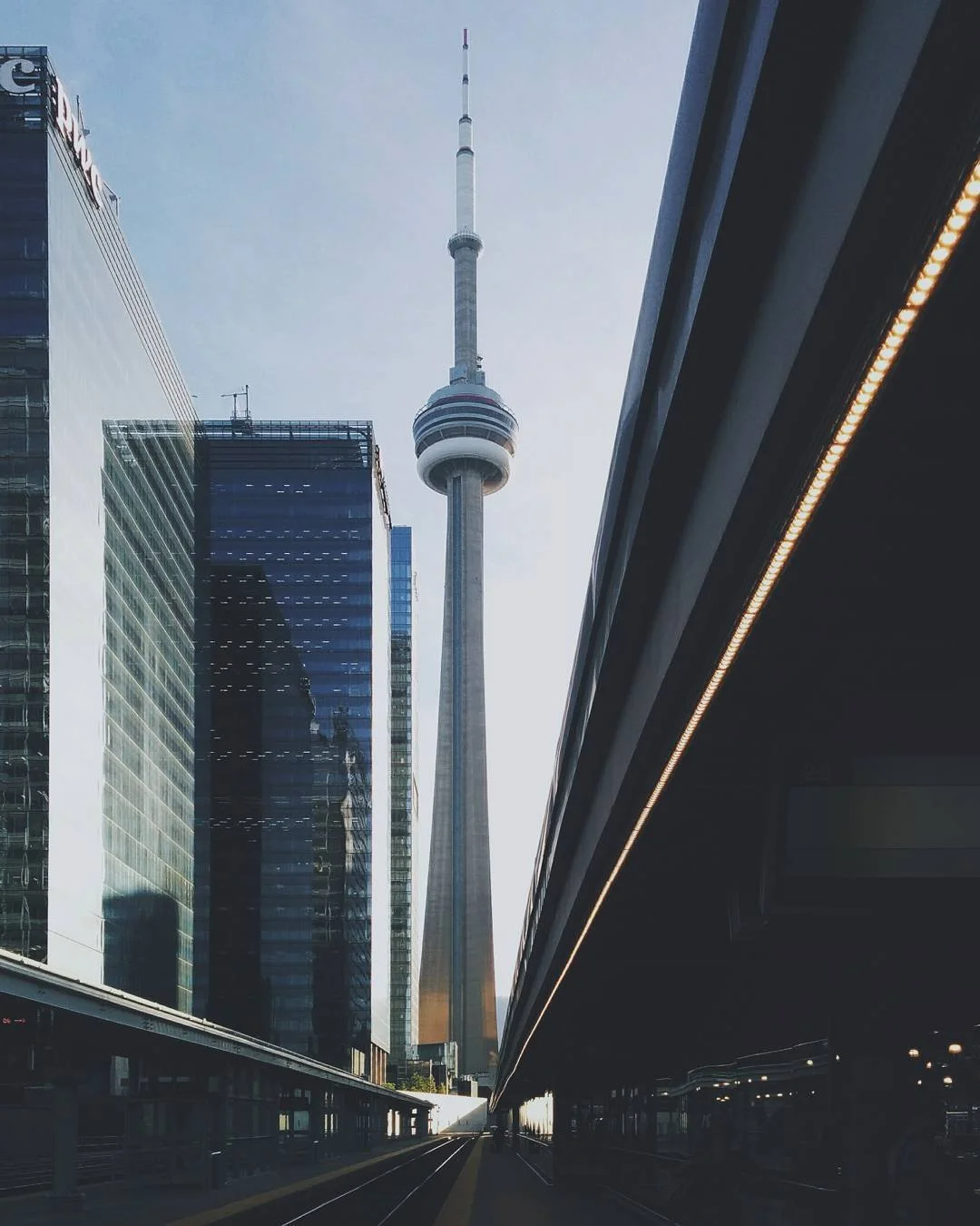 CN Tower and surrounding modern glass skyscrapers in Toronto, view from below with train tracks in foreground.
