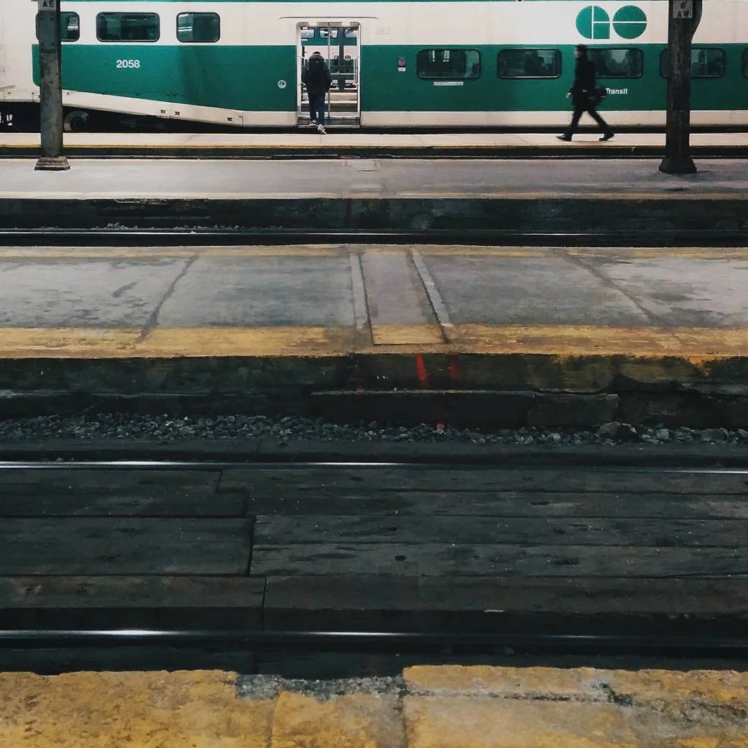 A green and white train at a station platform with two people walking or standing nearby.