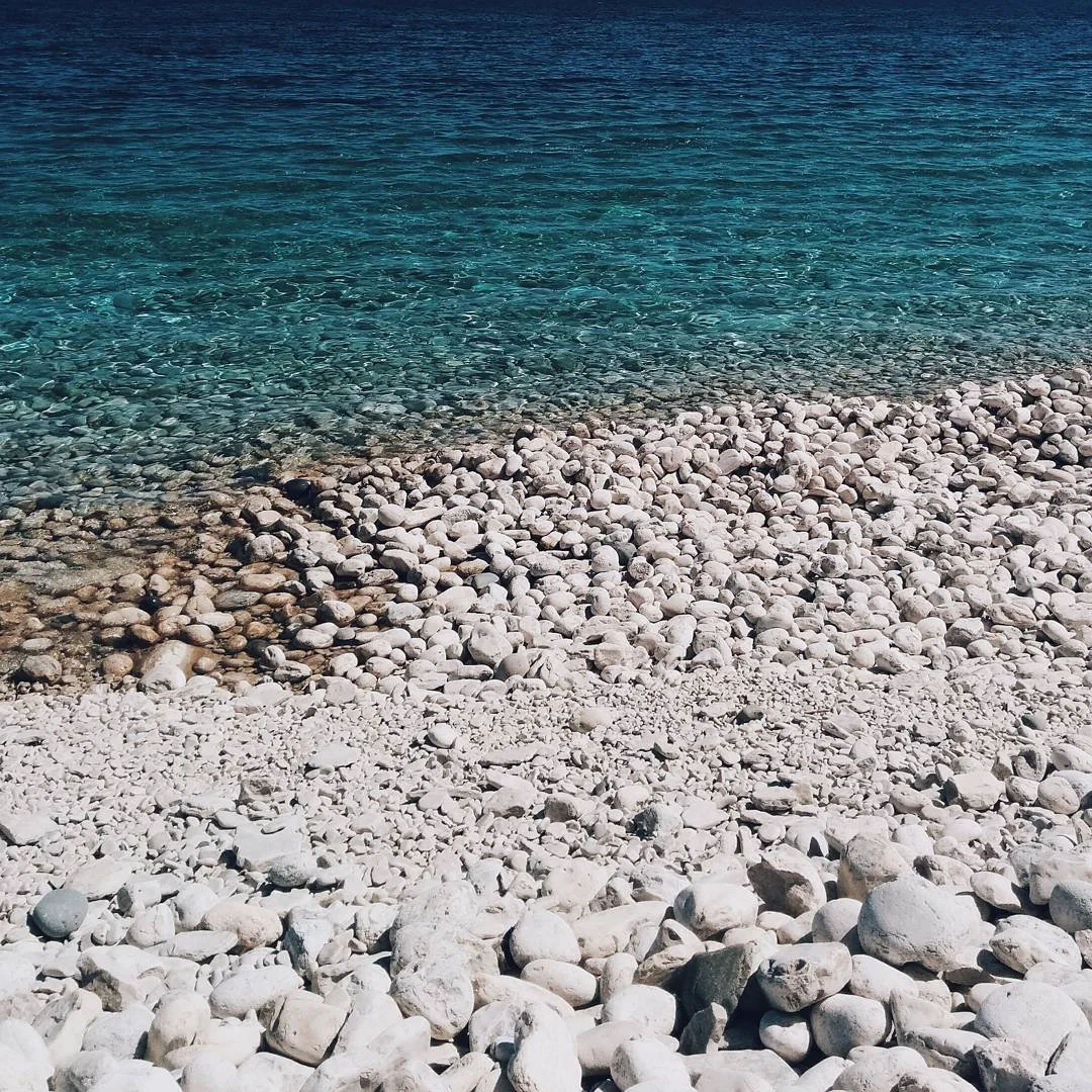 Rocky beach with clear blue water and a shoreline of white and gray stones.