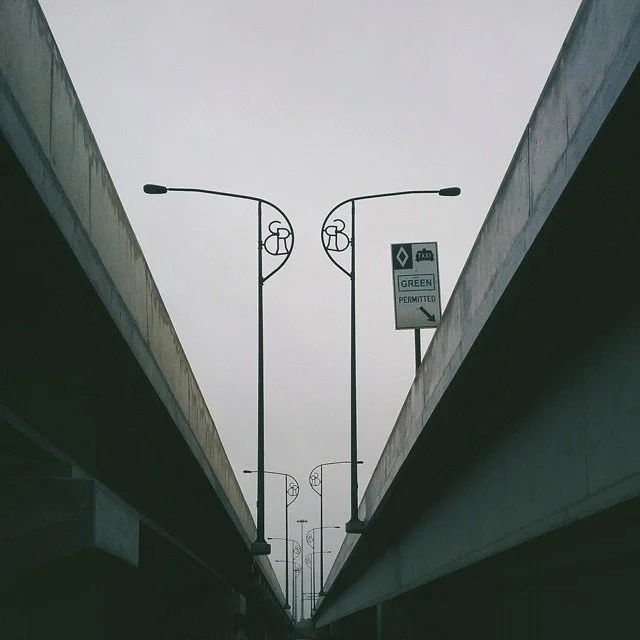 Looking up between two elevated highways with streetlights and a sign indicating permitted green lane.