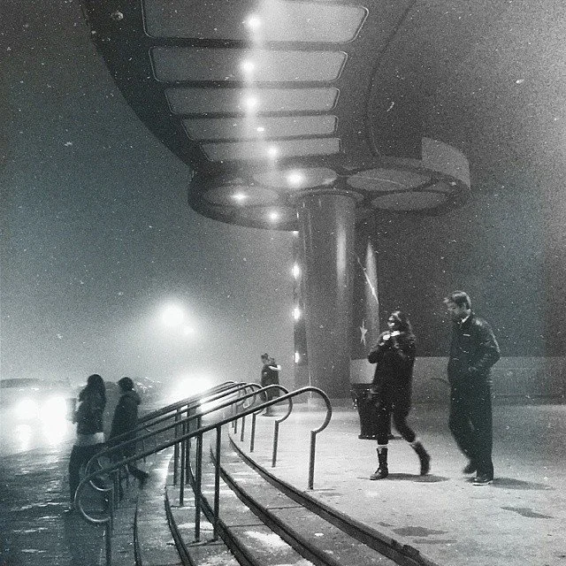 People walking in the snow under a large, illuminated canopy at night.