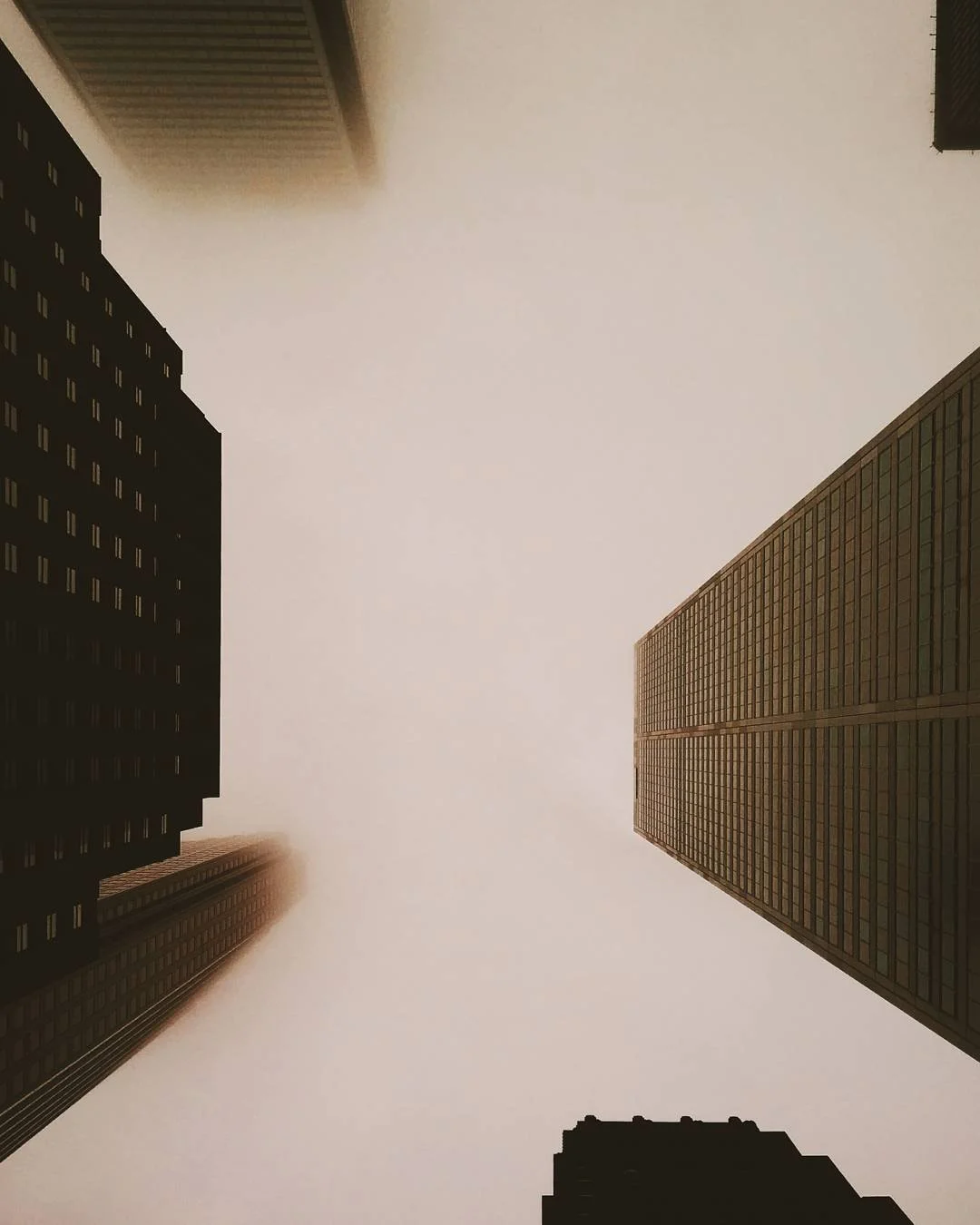 Looking up at tall skyscrapers in a city with a foggy or overcast sky.
