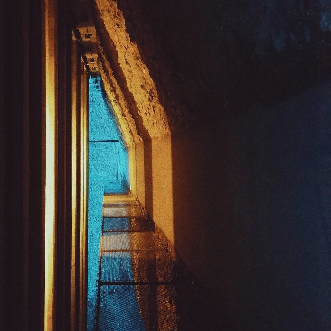 A view through a window showing a frozen pond with a small waterfall, surrounded by a fence at dusk or dawn.