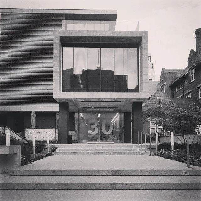 Modern building with large glass windowed cube on columns, with a staircase leading up to it, displaying the number '30' on the front and sign on the left indicating Gardiner P. A. O.