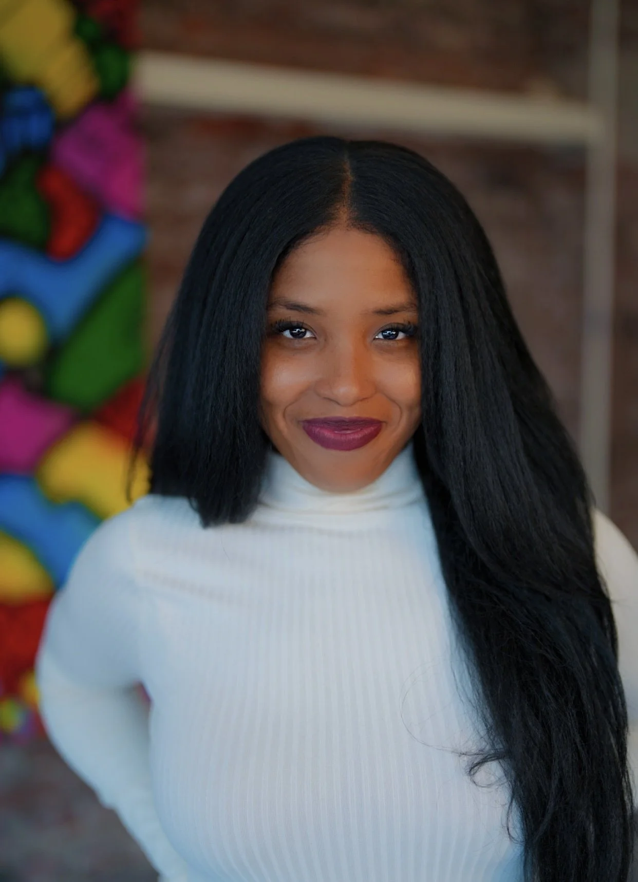 A feminine person with straight black hair and light brown skin smiles at the camera.