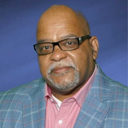 a Black man with a bald head wearing black rectangular glasses with gray facial hair