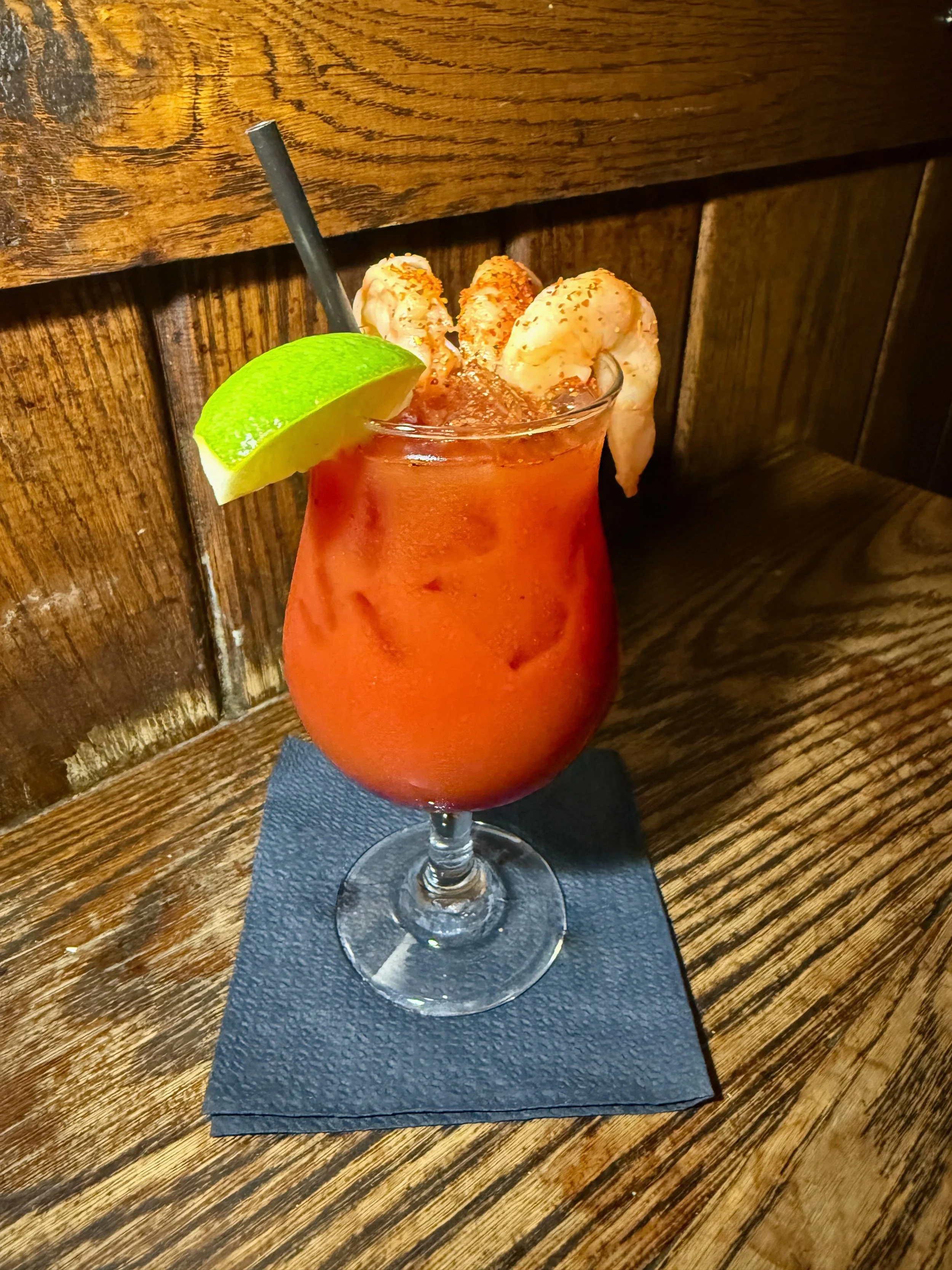 Achilles Heat Smoked Bloody Cantina made with our house Michelada Cantina mix, clam juice, tomato juice, Achilles Heat smoked hot sauce, topped off with sous vide Jumbo Shrimp Cocktail and a fresh lime wedge