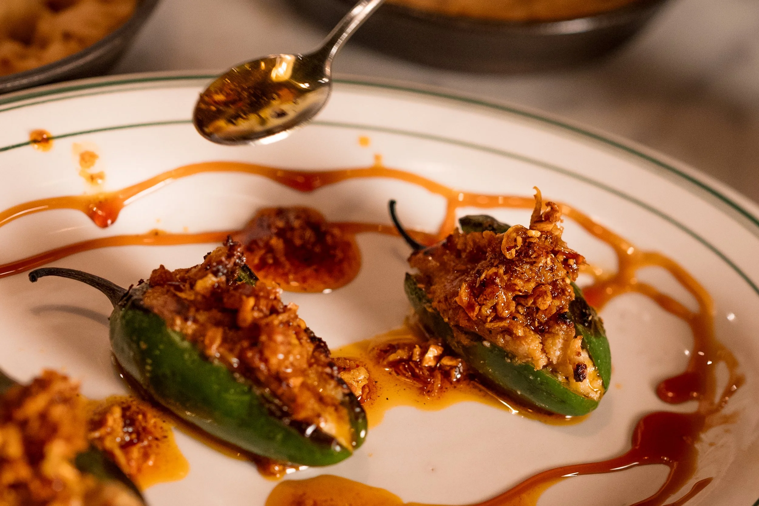 Paulie Gee's x Achilles Heat: Wood-fired jalapenos stuffed with Paulie Gee's cashew ricotta and NUMU mozzarewlla, blended with Achilles Heat Smoked Chili Crisp, drizzled with balsamic reduction, and finished with even more smoked chili crisp for extr