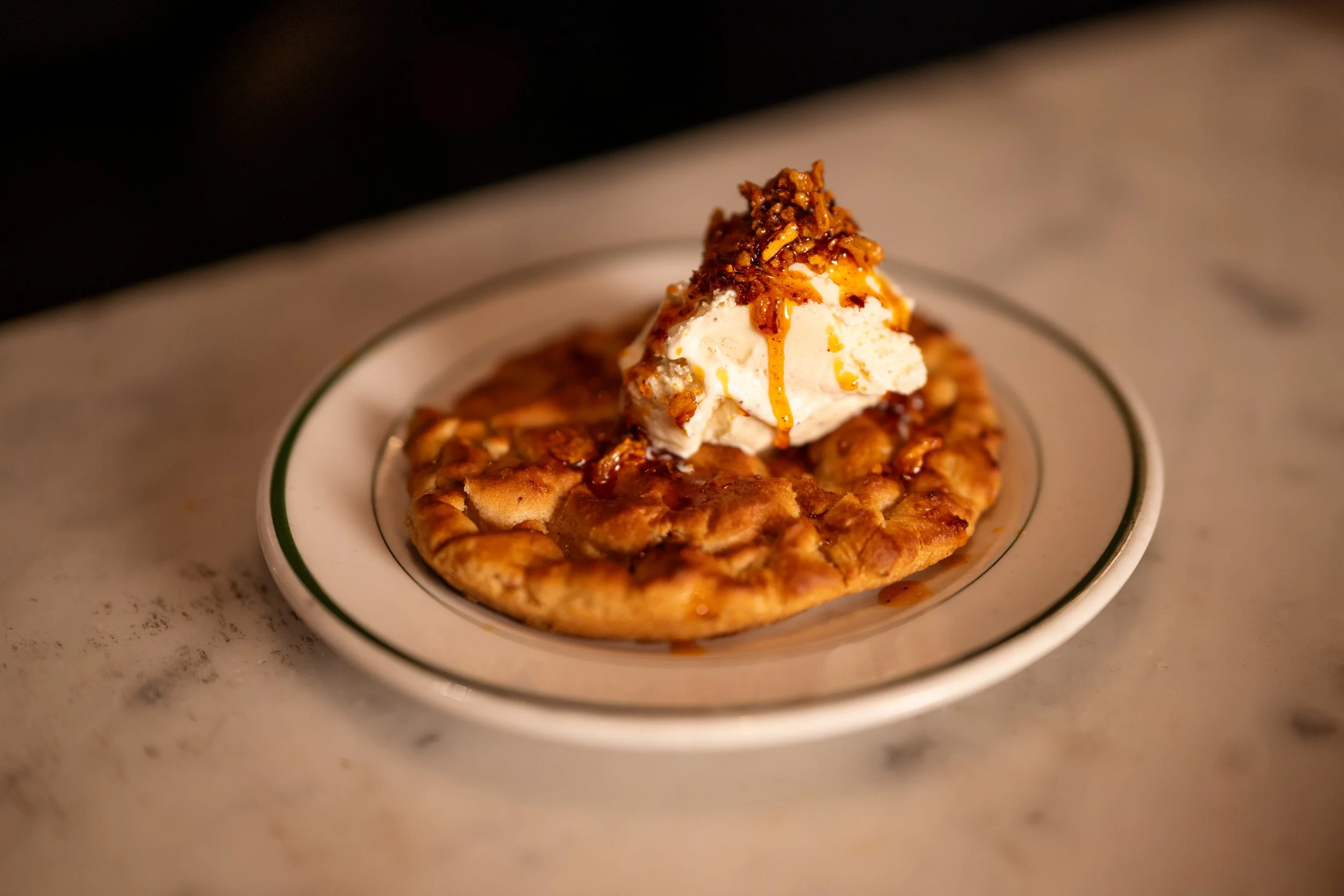 Warm wood fired Marscapone sugar cookie topped off with Van Leeuwen vanilla bean ice cream and topped with a generous drizzle of Achilles Heat smoked chili crisp, by Chef Marney Rose of Paulie Gee's Restaurant