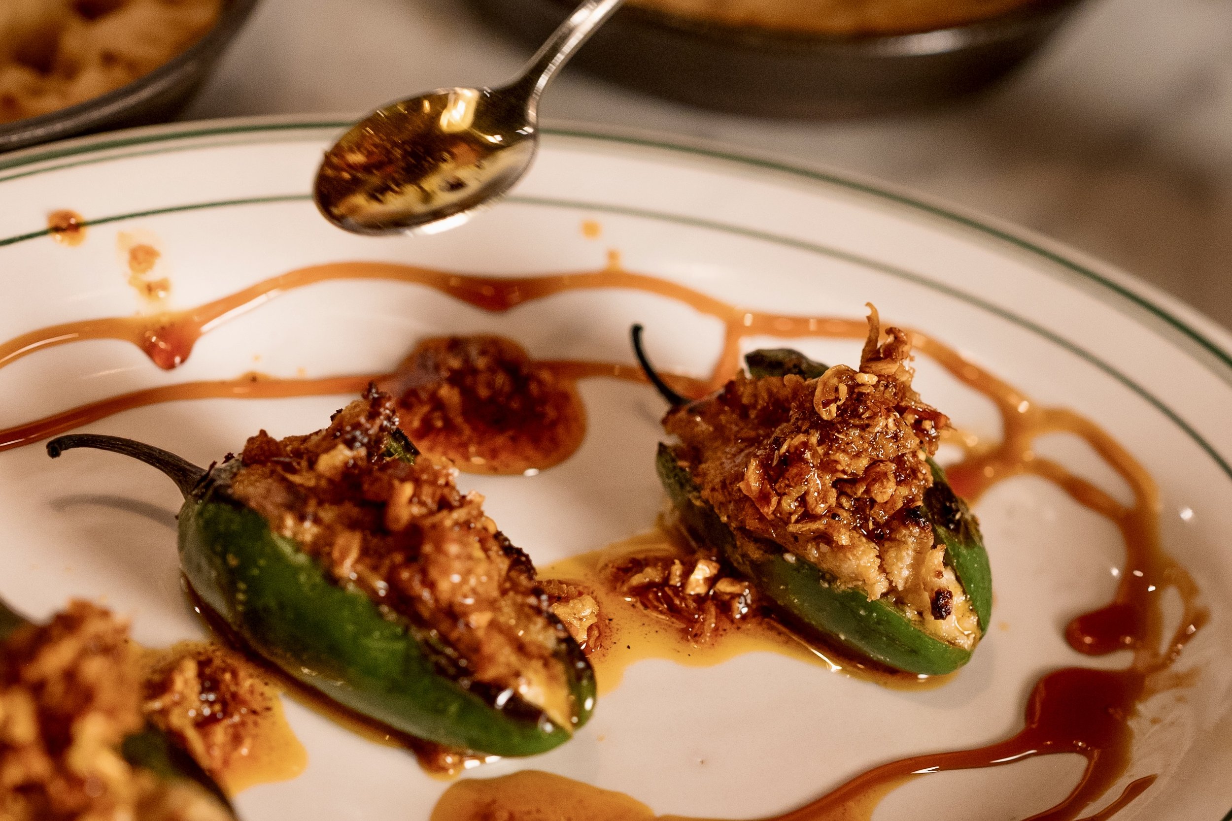 Close-up of stuffed jalapeño peppers topped with chopped nuts or breadcrumbs and drizzled with barbecue sauce on a white plate.
