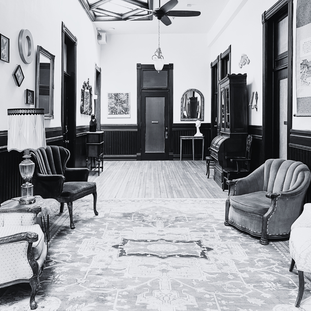 A vintage living room with antique furniture, framed artwork, a columned door, and a patterned area rug in black and white.