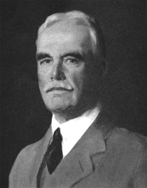 Black and white portrait of a serious-looking man in a suit and tie with neatly combed hair and a mustache.