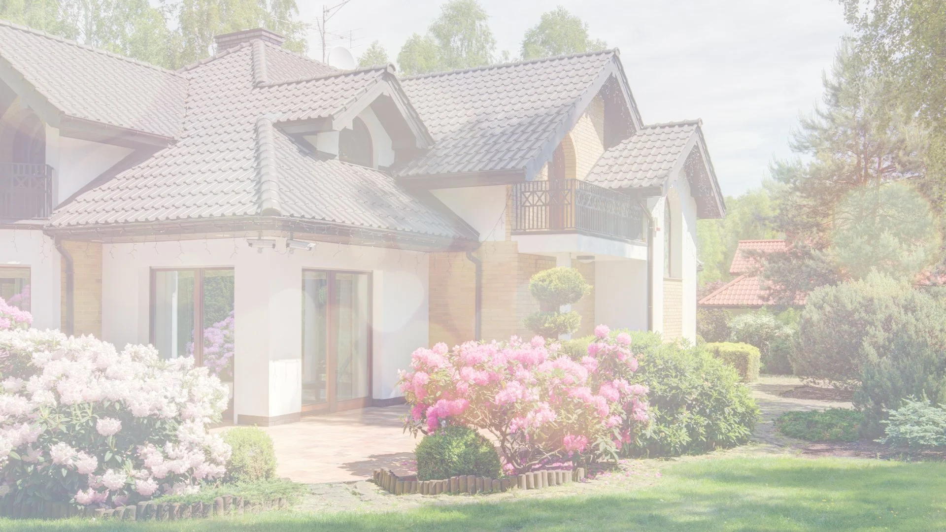 House with a tiled roof surrounded by blooming pink and white flowers in a garden.