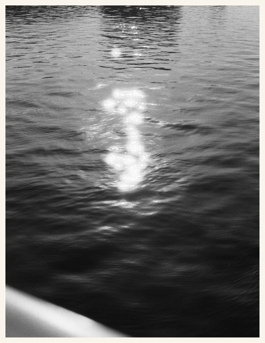 Reflection of sunlight on the surface of a body of water, with ripples and a portion of a boat or structure at the bottom corner.
