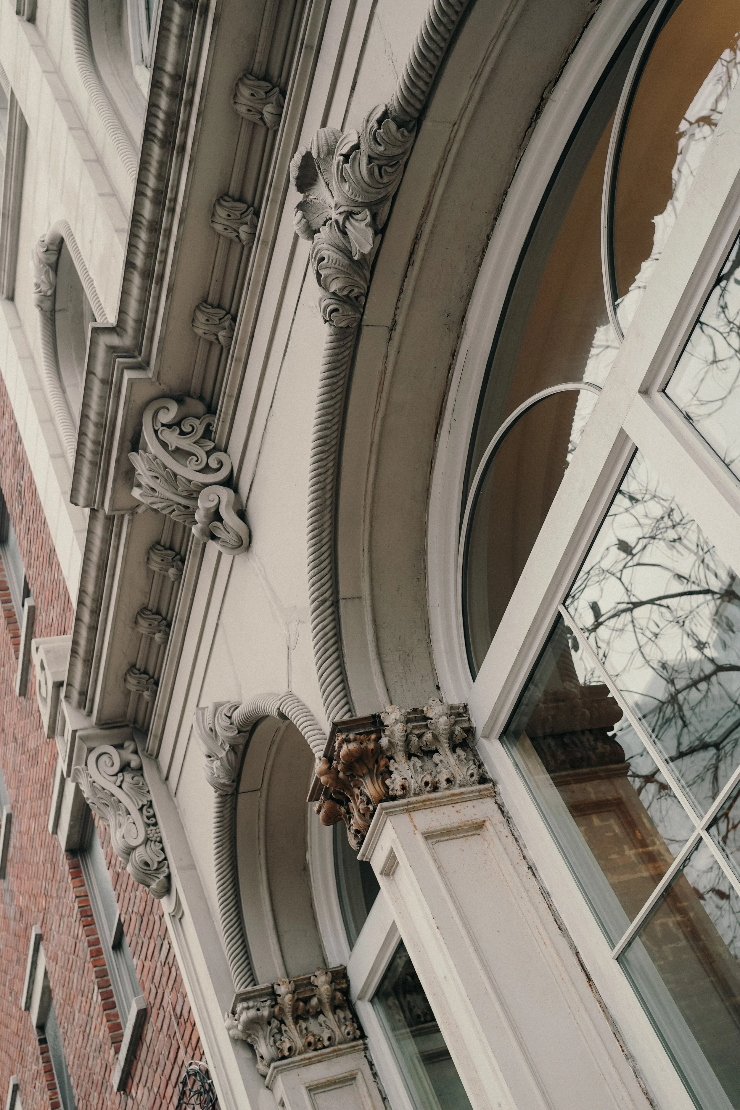 Close-up of an ornate building facade with decorative molding, columns, and large arched windows, showing signs of weathering and some peeling paint.
