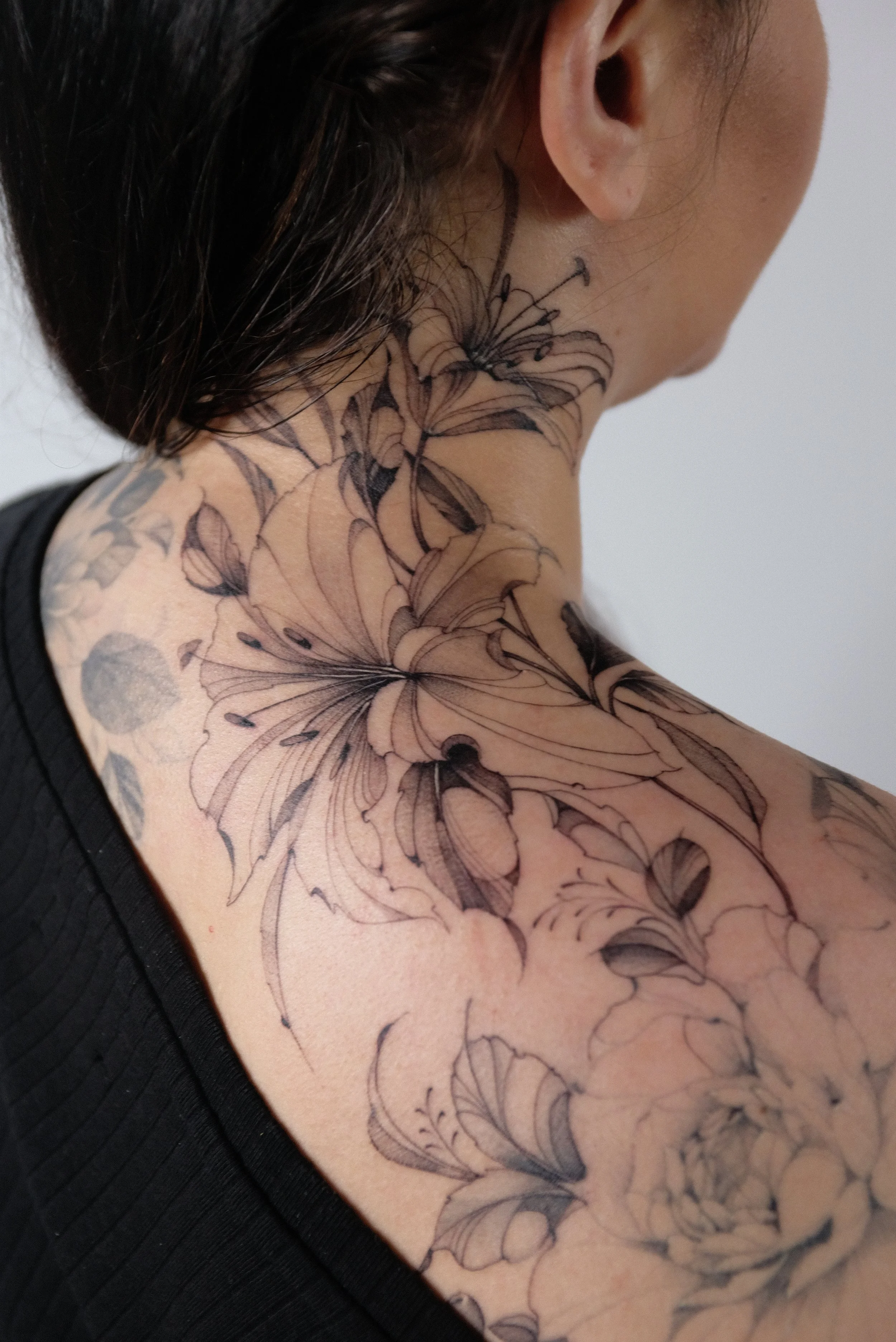 Close-up of a person's neck, shoulder, and upper chest showing a detailed black ink floral tattoo.