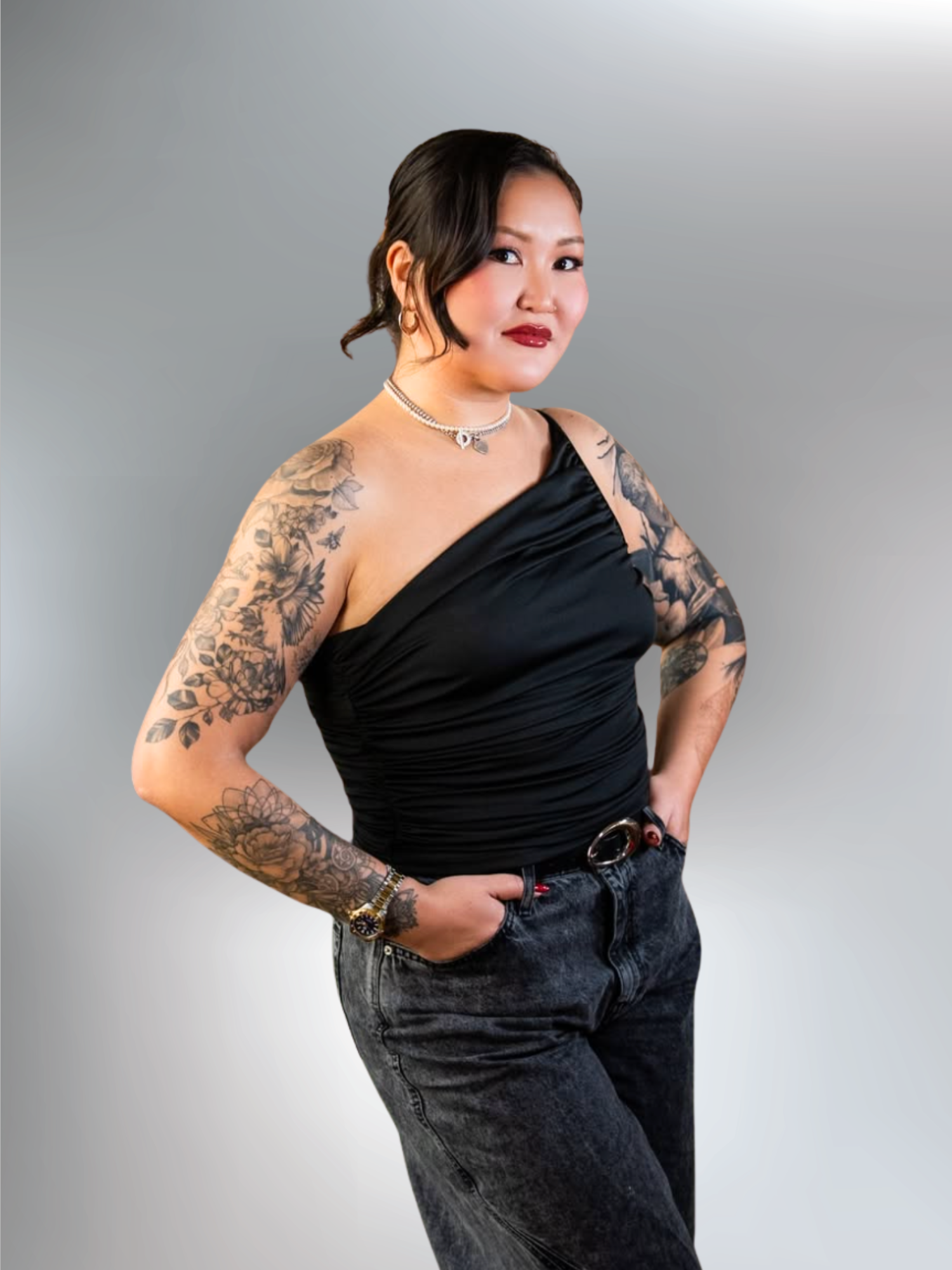 A woman with dark hair styled in an updo, wearing a pearl necklace, denim jean and an asymmetrical top.