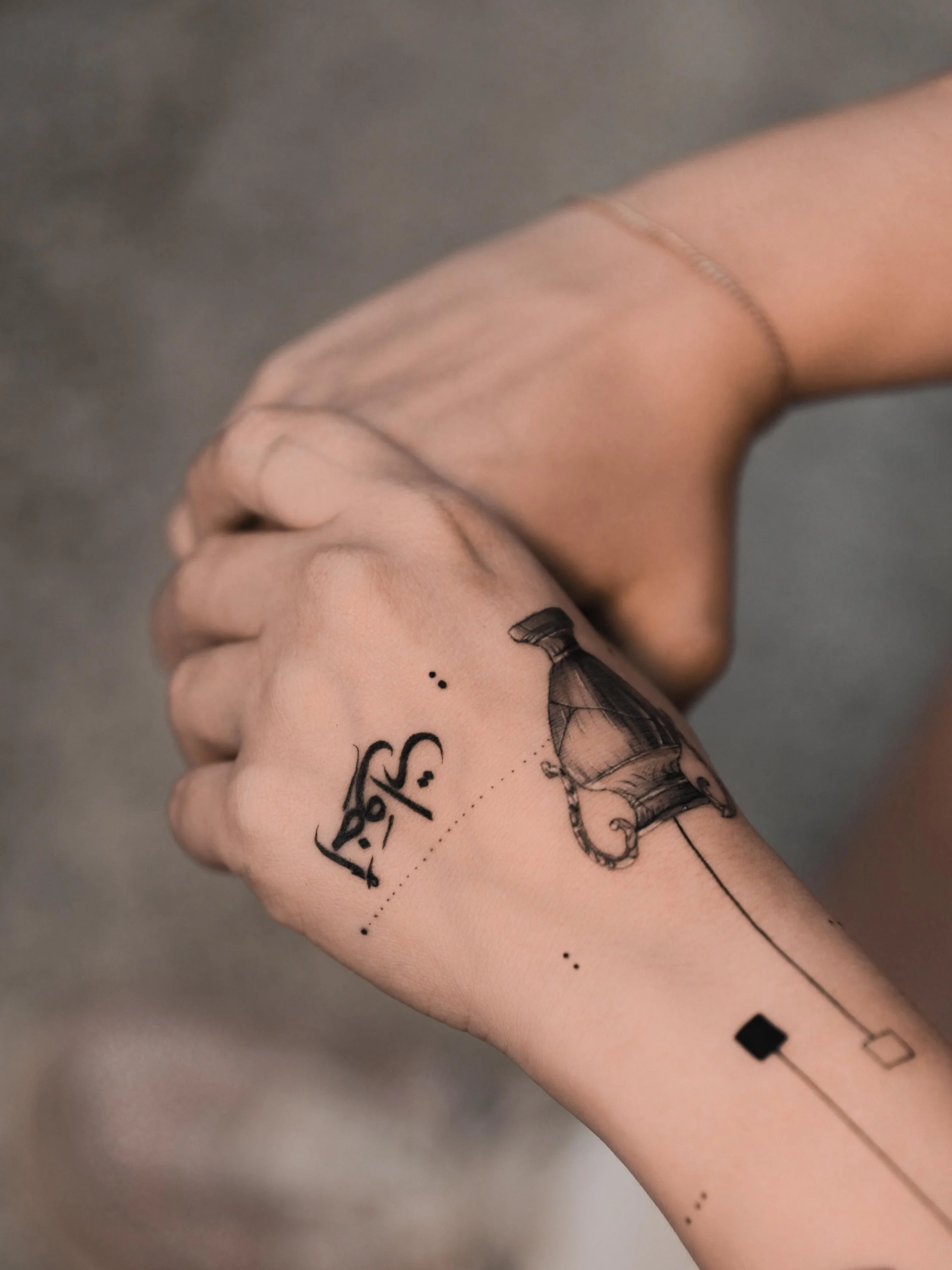 Close-up of a person's hand with tattoos, including a lighthouse, dotted lines, and abstract symbols.