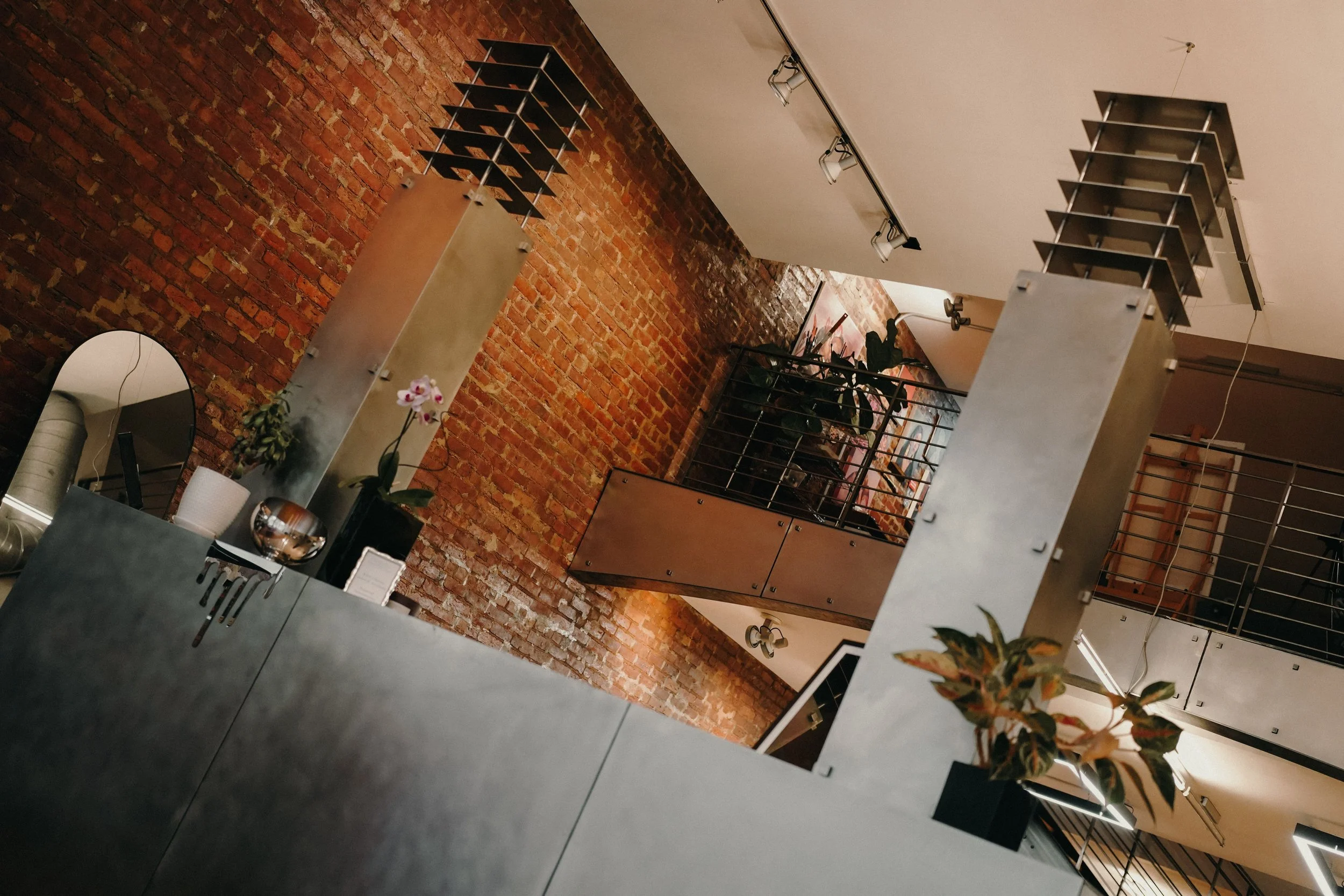 Interior of a modern industrial-style building with brick walls, metal columns, plants, and a mezzanine level.