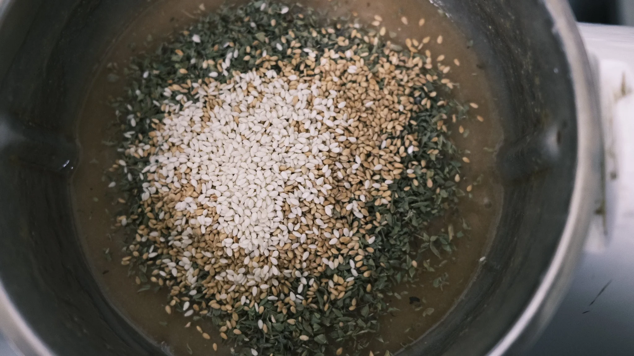 A close-up view of a blender container filled with sesame seeds and chopped herbs.
