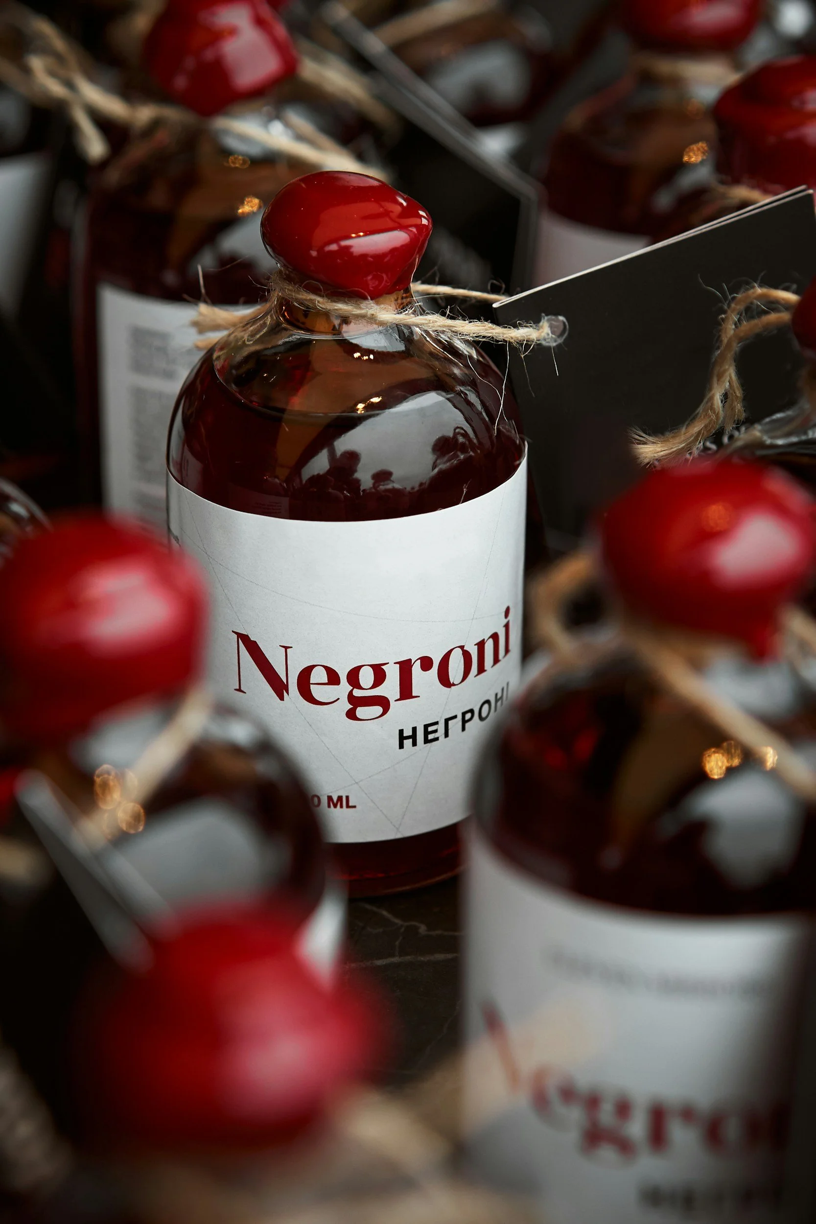 Bottles of Negroni liqueur with red caps and white labels, surrounded by other similar bottles, on a dark surface.