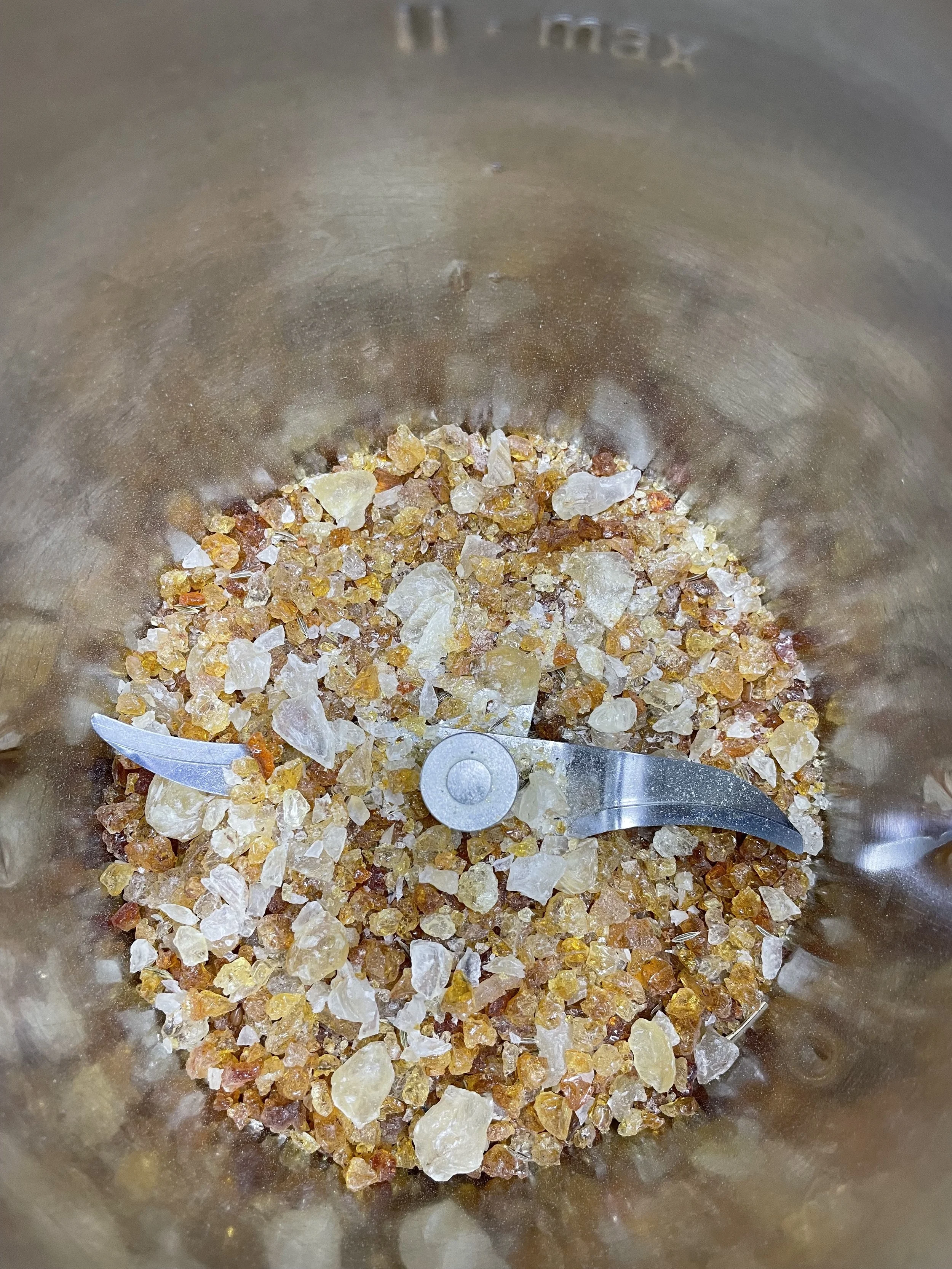 Close-up of a food processor bowl containing crushed amber-colored stones.