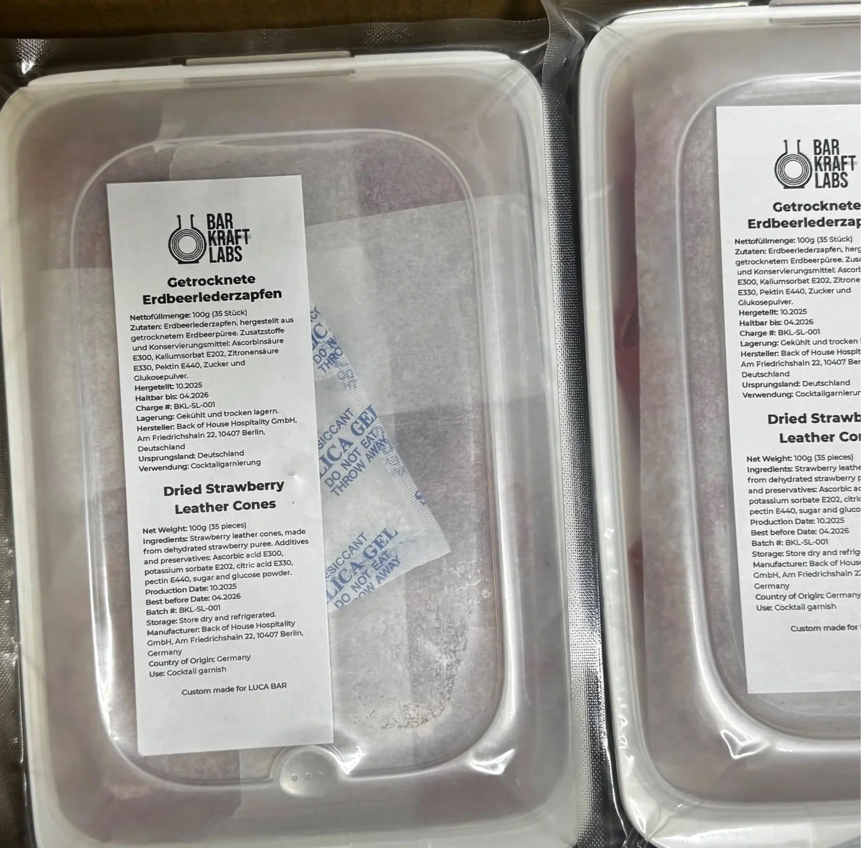 Two plastic containers with labels listing ingredients and details of strawberry leather cones, including weight, ingredients, and manufacturer.