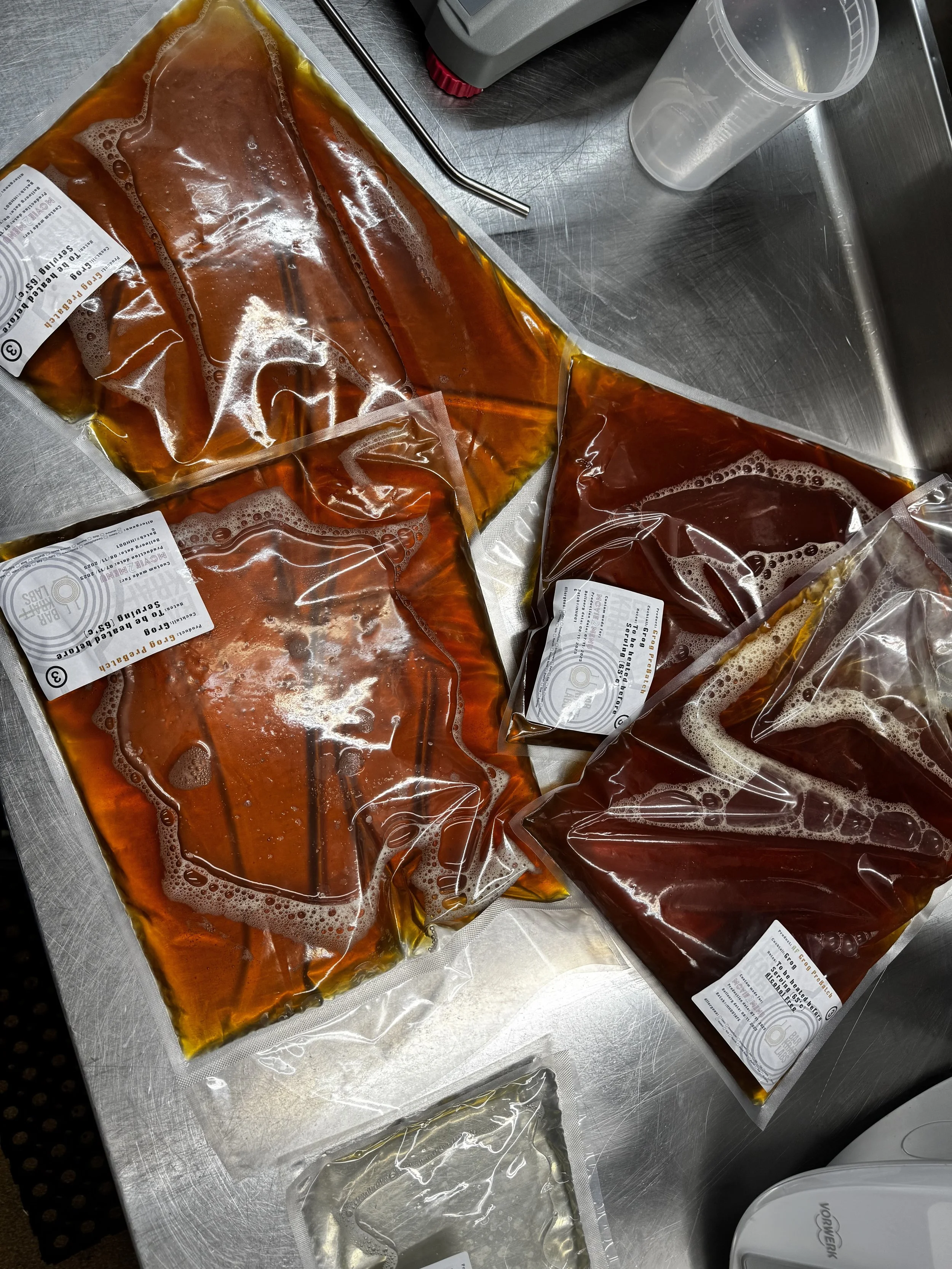 Three vacuum-sealed bags of liquid, likely blood, on a stainless steel surface in a laboratory setting.