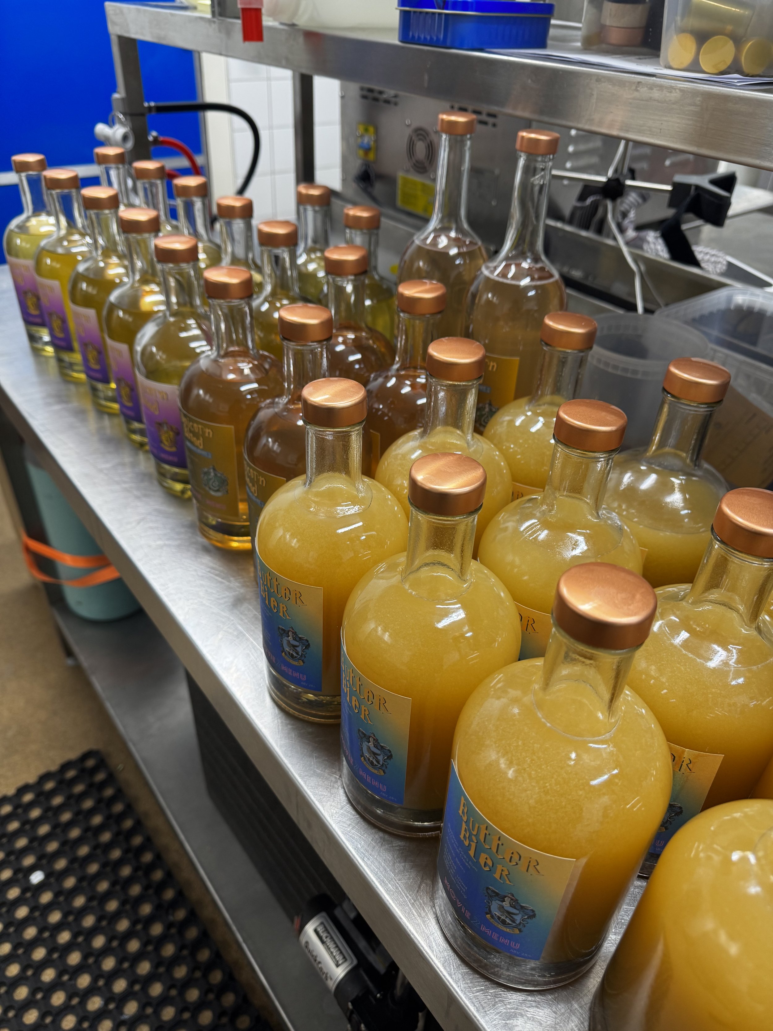 Bottles of yellow liquid on a stainless steel table in a kitchen or lab environment.