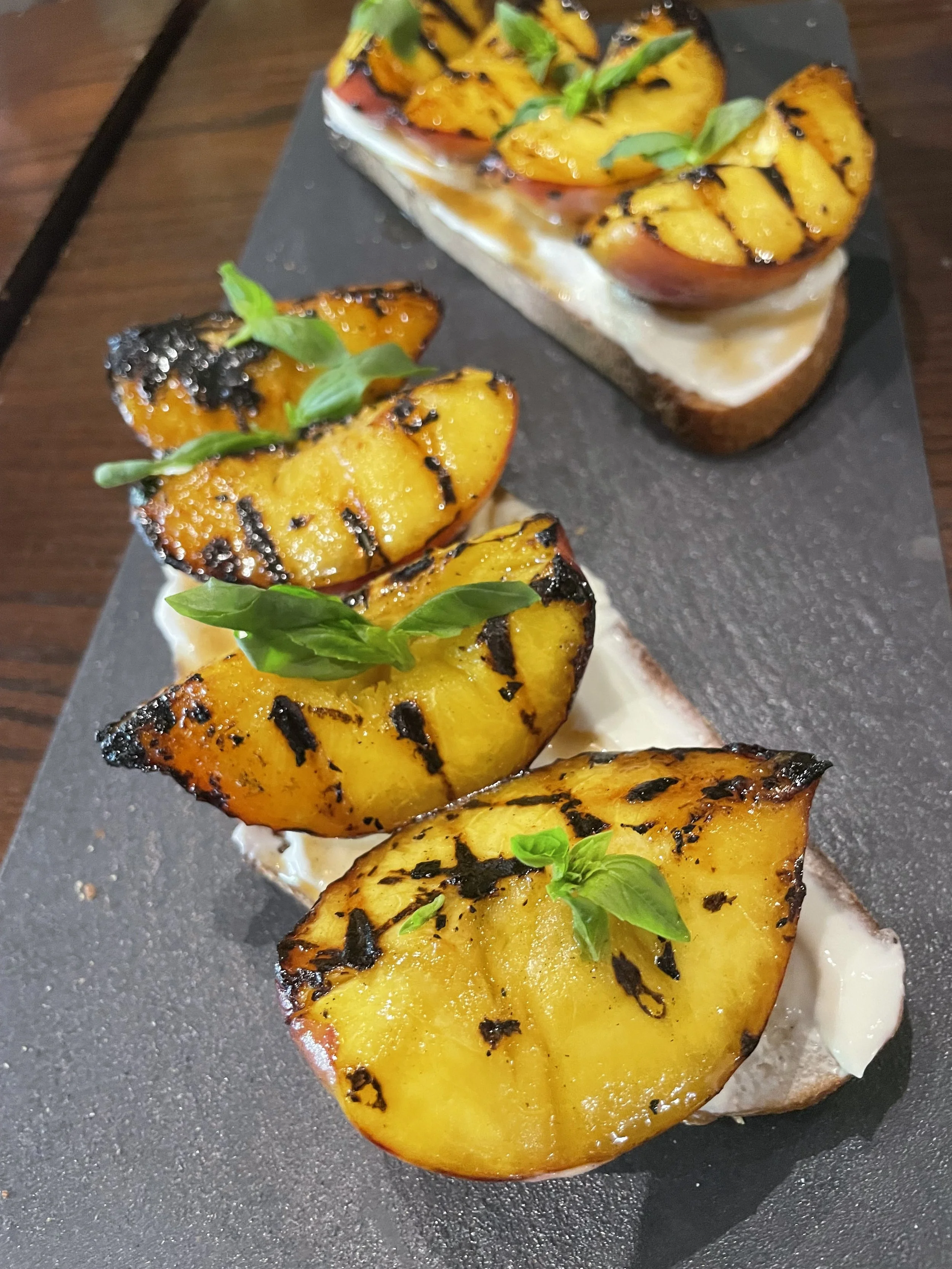 Grilled peach slices garnished with basil leaves, served on toast with a layer of cream cheese or similar spread.