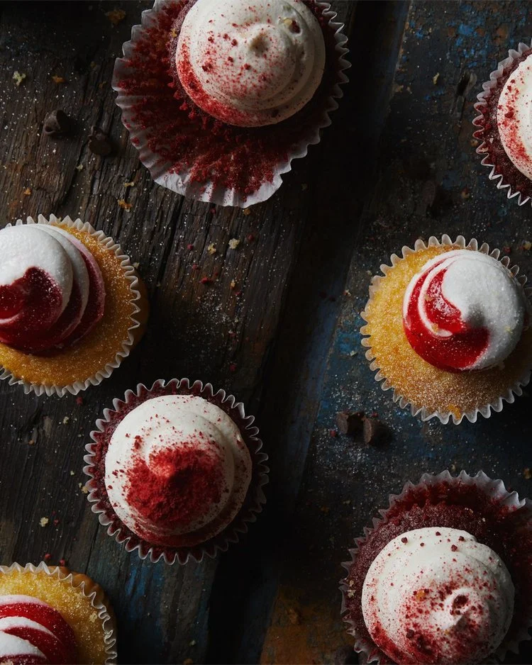 Cupcakes with white frosting and red sprinkles, topped with red swirl decorations, on a rustic wooden surface.