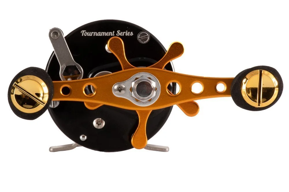 Close-up of a fishing reel with a black base, orange handle, and gold accents.