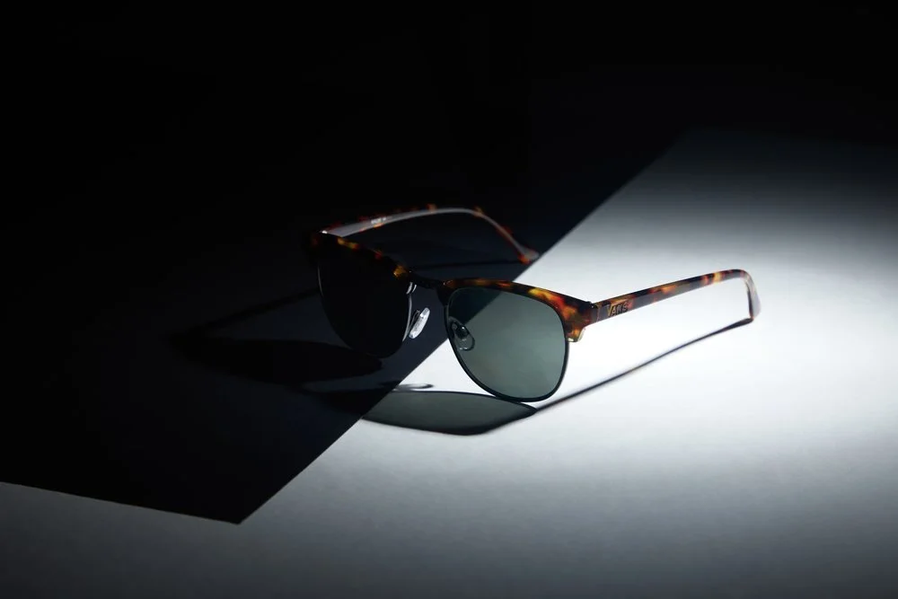 A pair of tortoiseshell sunglasses with dark lenses, placed on a surface divided between darkness and light, casting shadows.